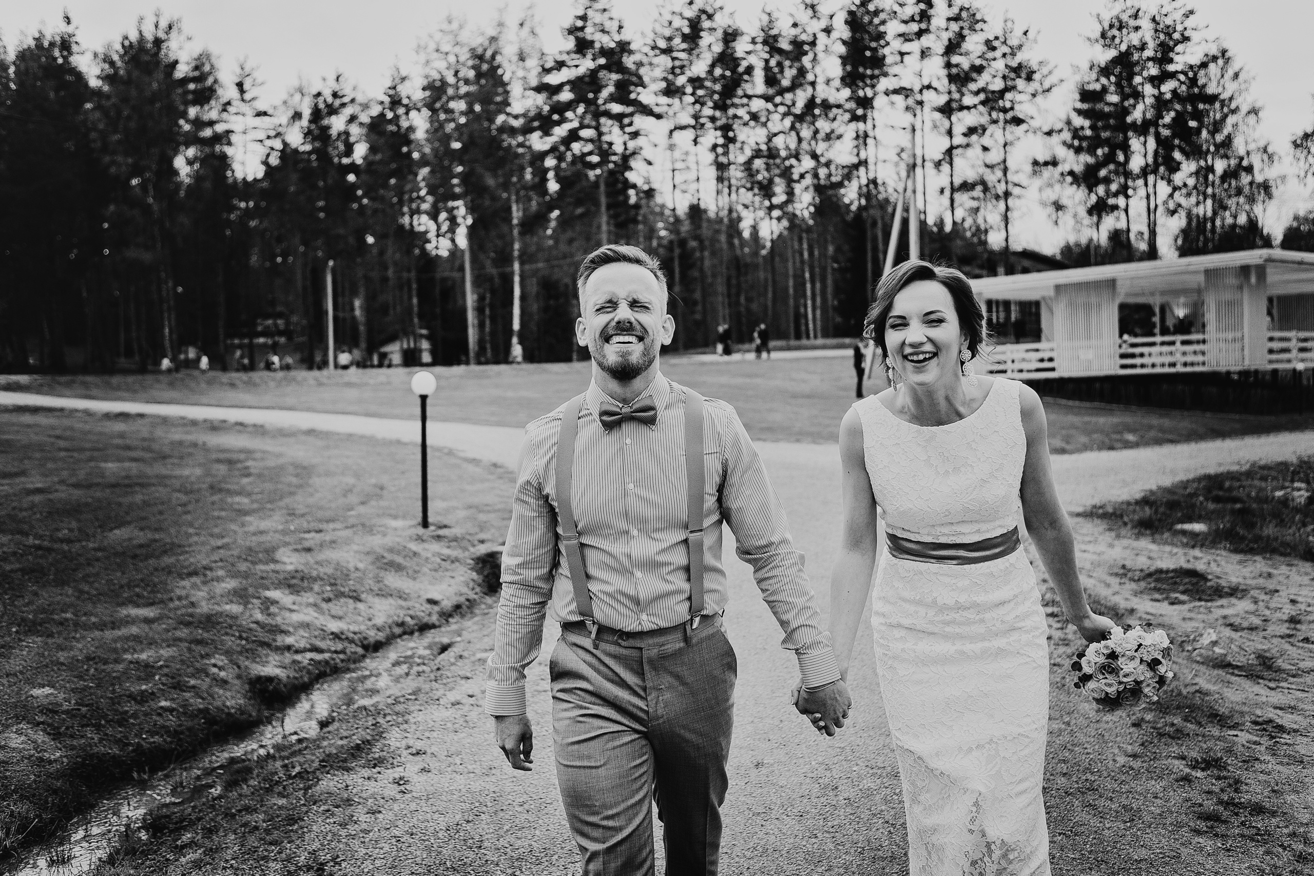 смеющаяся пара идет взявшись за руки по дорожке в парке