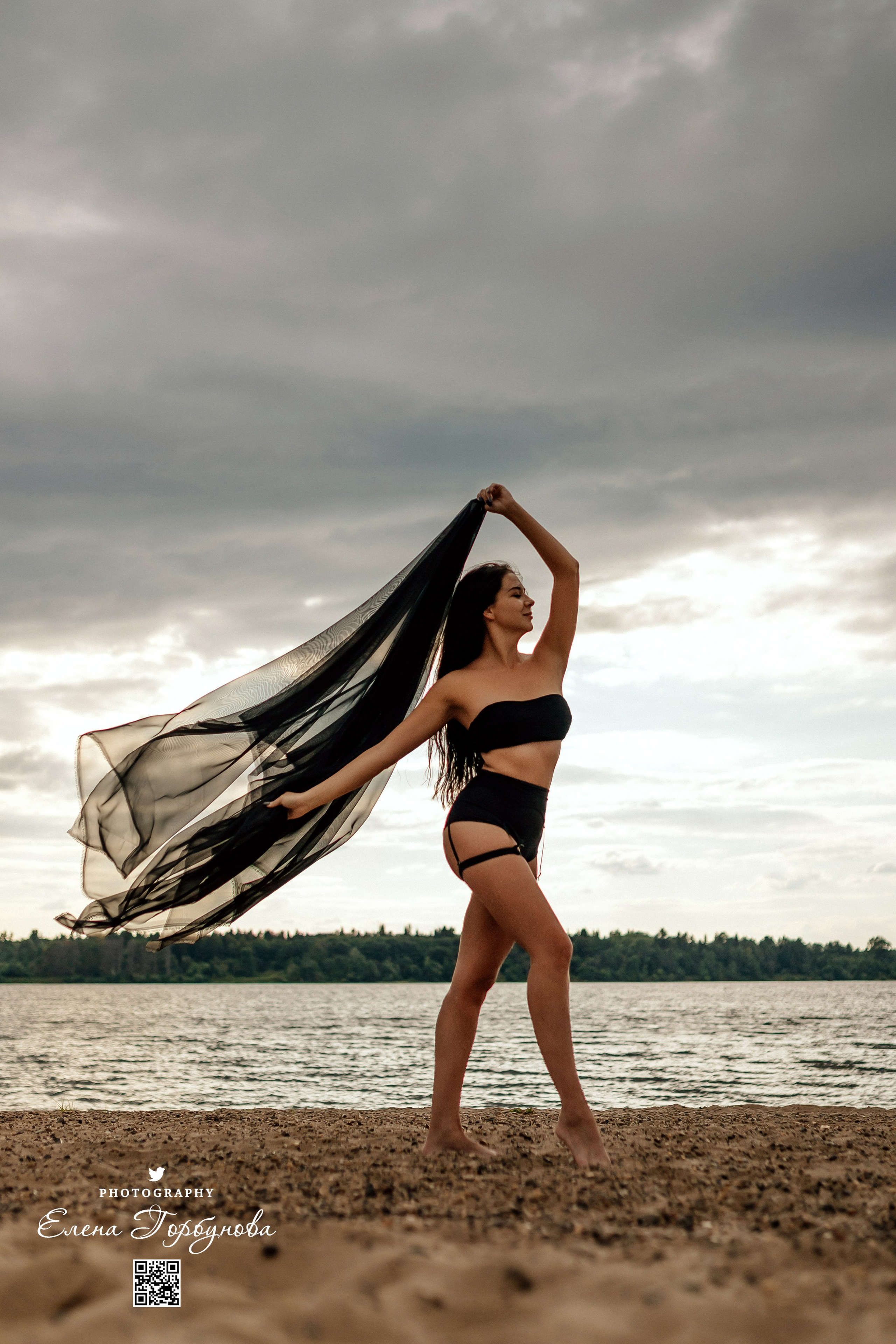 Фотосессия с черной тканью. Легкая черная вуаль летит на вертру. Фотосессия у реки черная серия с тканью. Девушка укуталась в черную ткань. Прогулка по набережной. Песок, речка, модель в черном. Качели над водой, Закат. Девушка лежит на песке. В зеленых деревьях