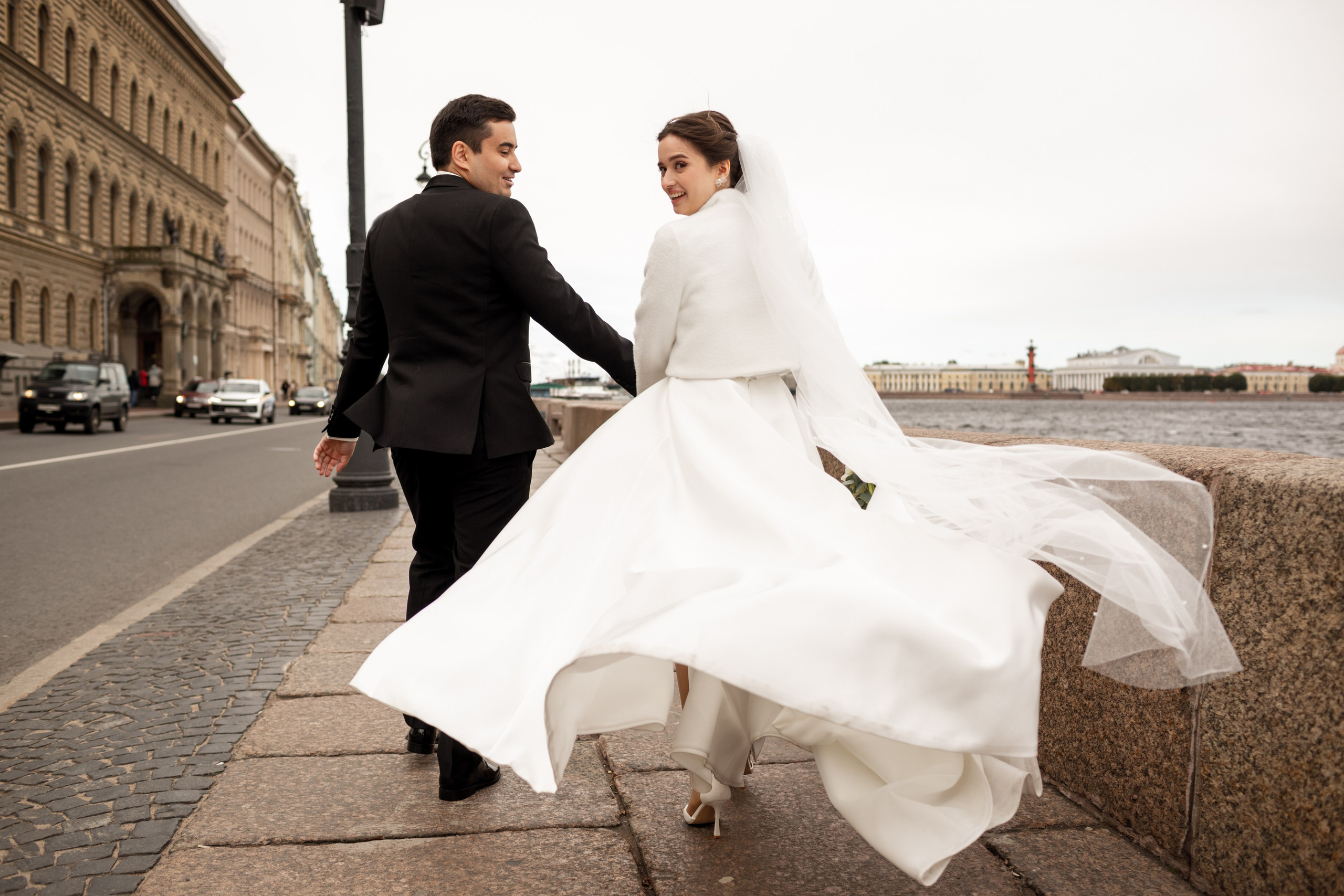 Живой кадр: жених и невеста бегают по набережной Петербурга, подол развевается на ветру.