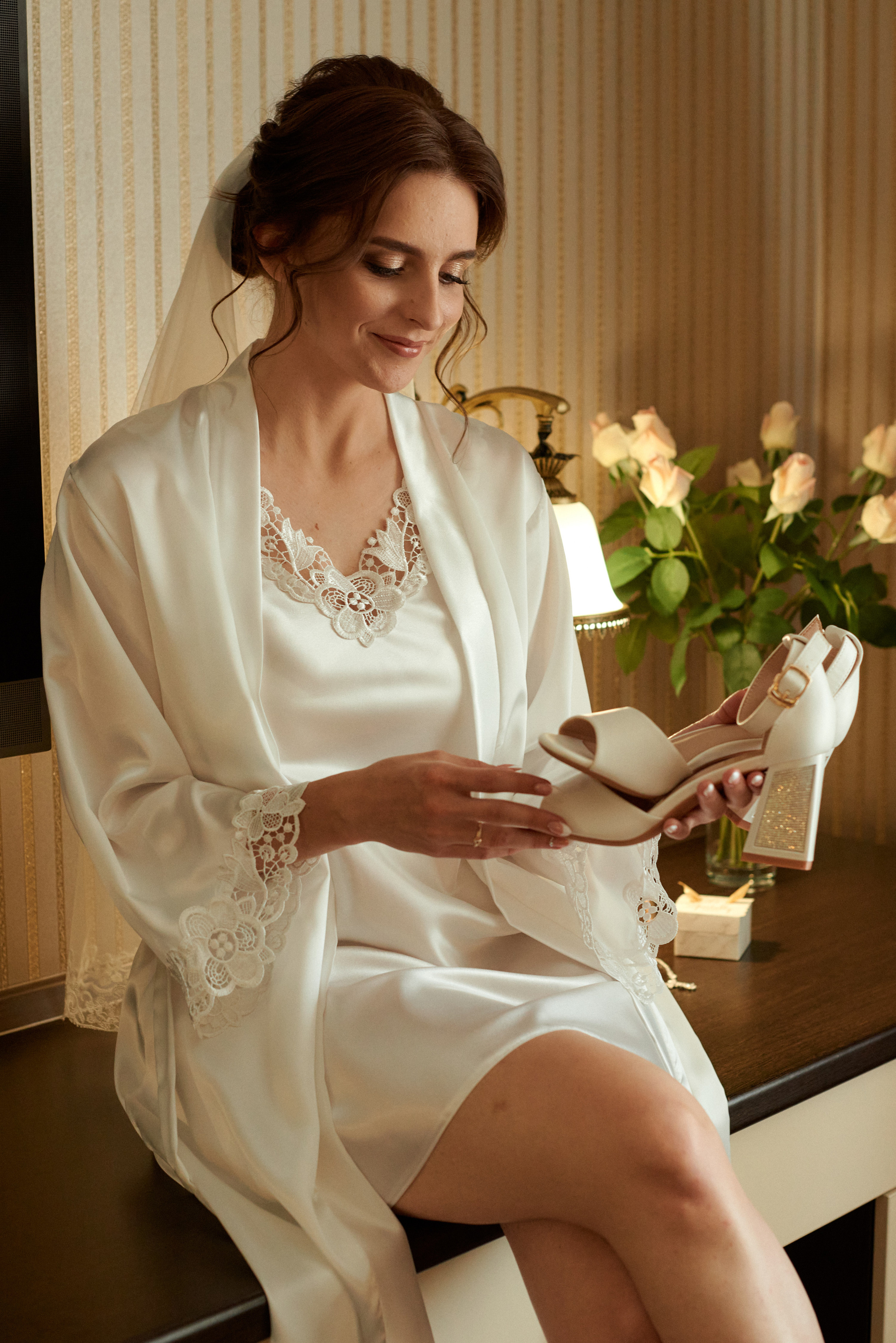 Утро невесты. Невеста в пеньюаре сидя на столе рассматривает свои свадебные туфли.