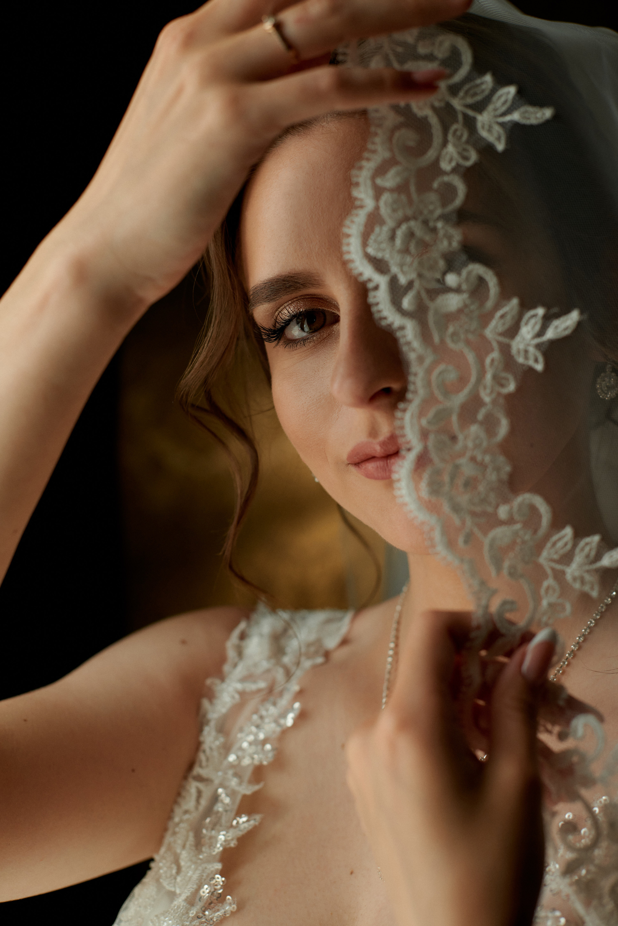 Невеста закрывает пол лица кружевом фаты.