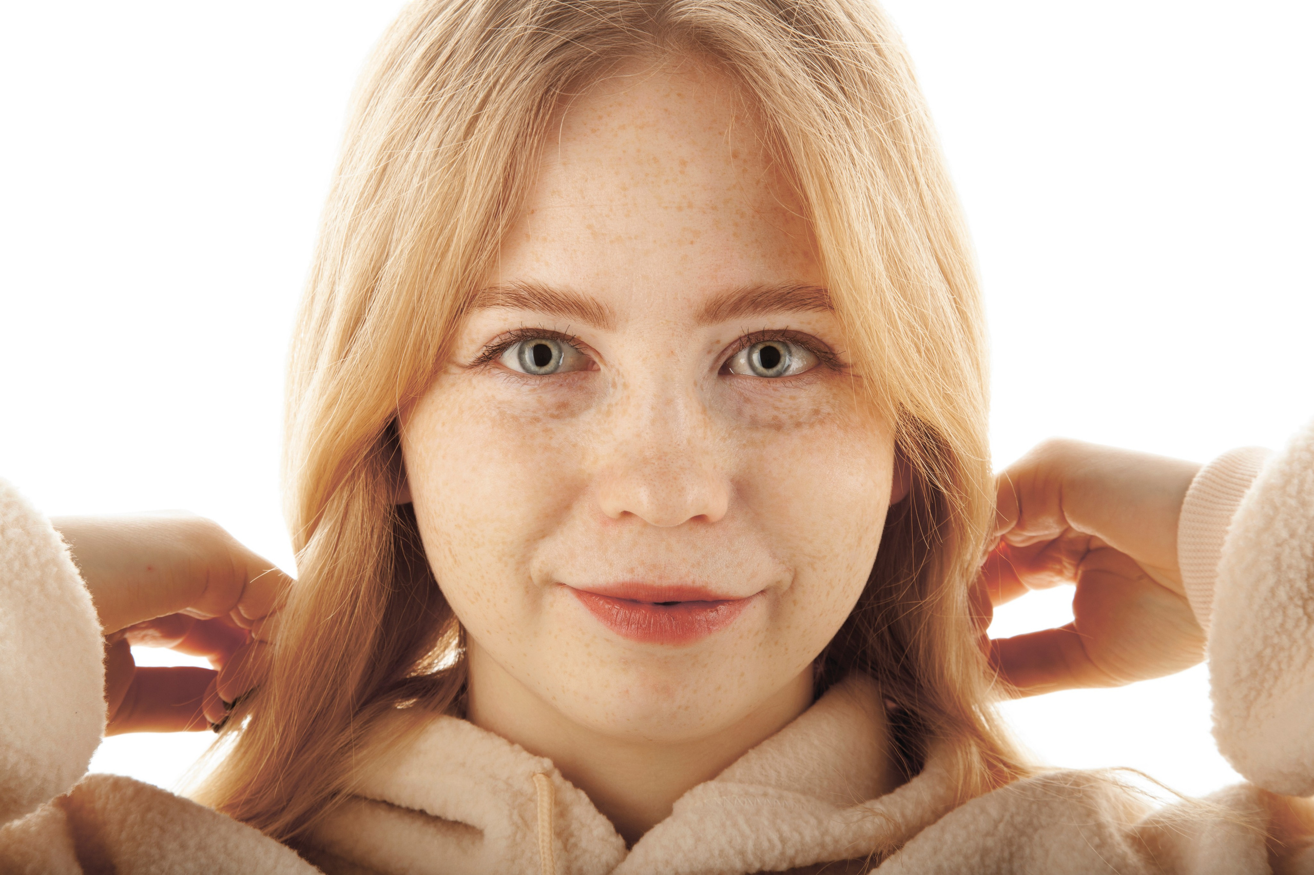 Портрет светловолосой и голубоглазой девушки с веснушками. В светлой одежде на белом фоне.