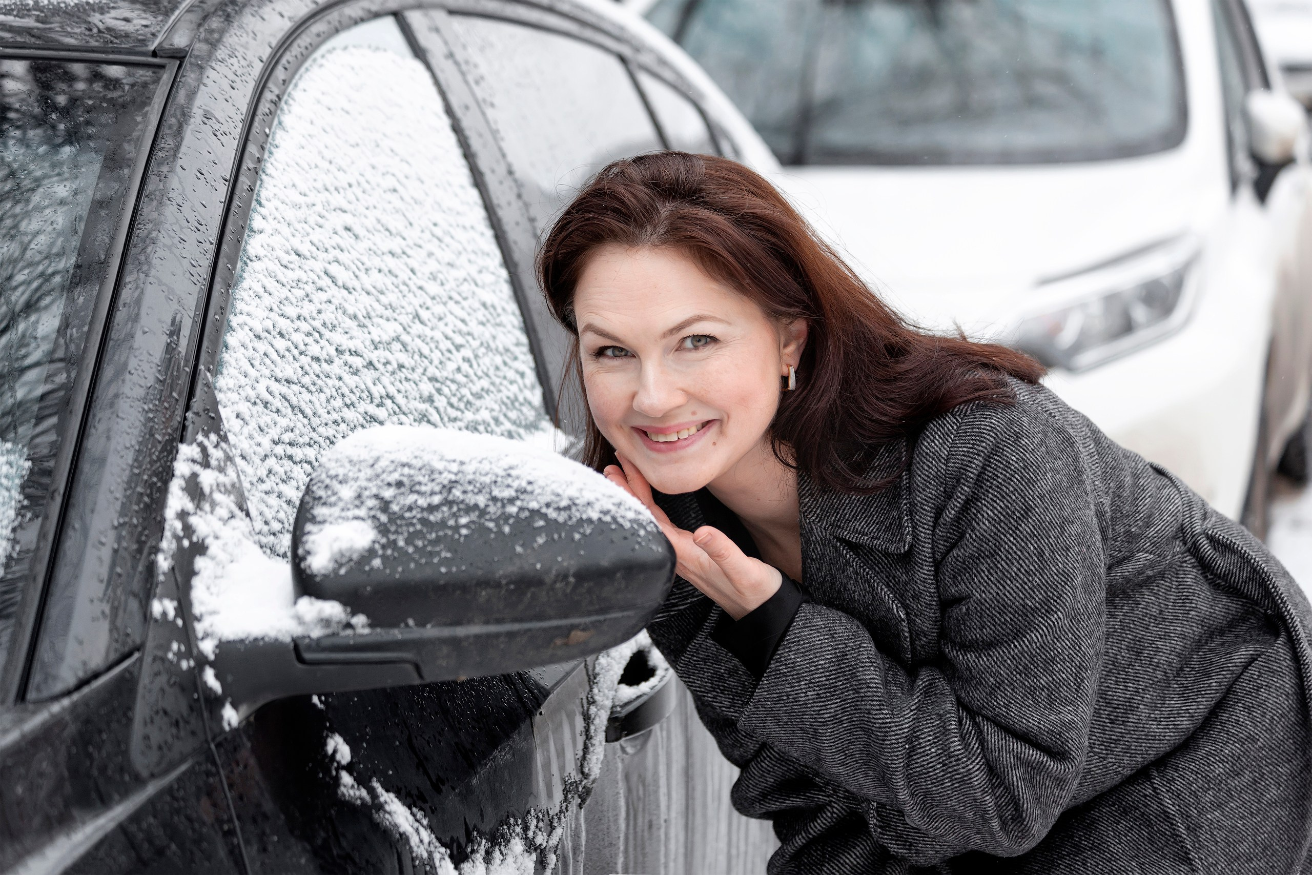 Девушка смотрится в зеркало заднего вида припаркованного авто