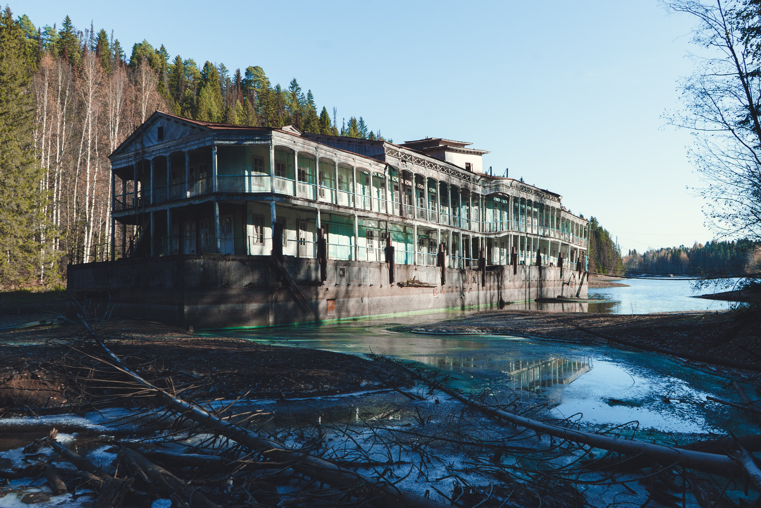 Заброшенное здание, виднеющееся на старинном берегу речной пароход, стоит на водоеме среди густого леса. Его фасад украшен колоннами и балконами, однако здание выглядит ветхим и запущенным: краска облупилась, металл покрыт ржавчиной. Вокруг голые деревья и хвойные леса, что создает ощущение уединенности и застенчивости.