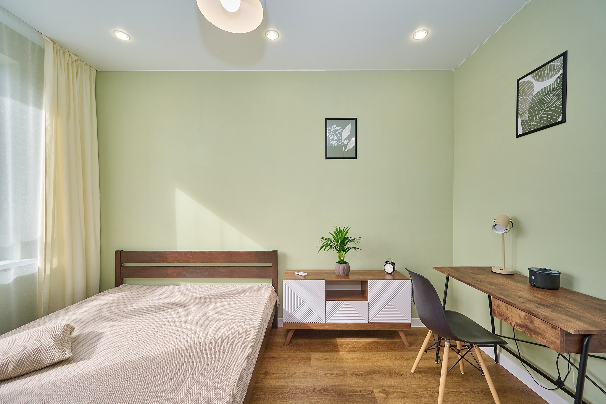 комната салатовые стены коричневый стол со стулом белые полки кровать светлые шторы 