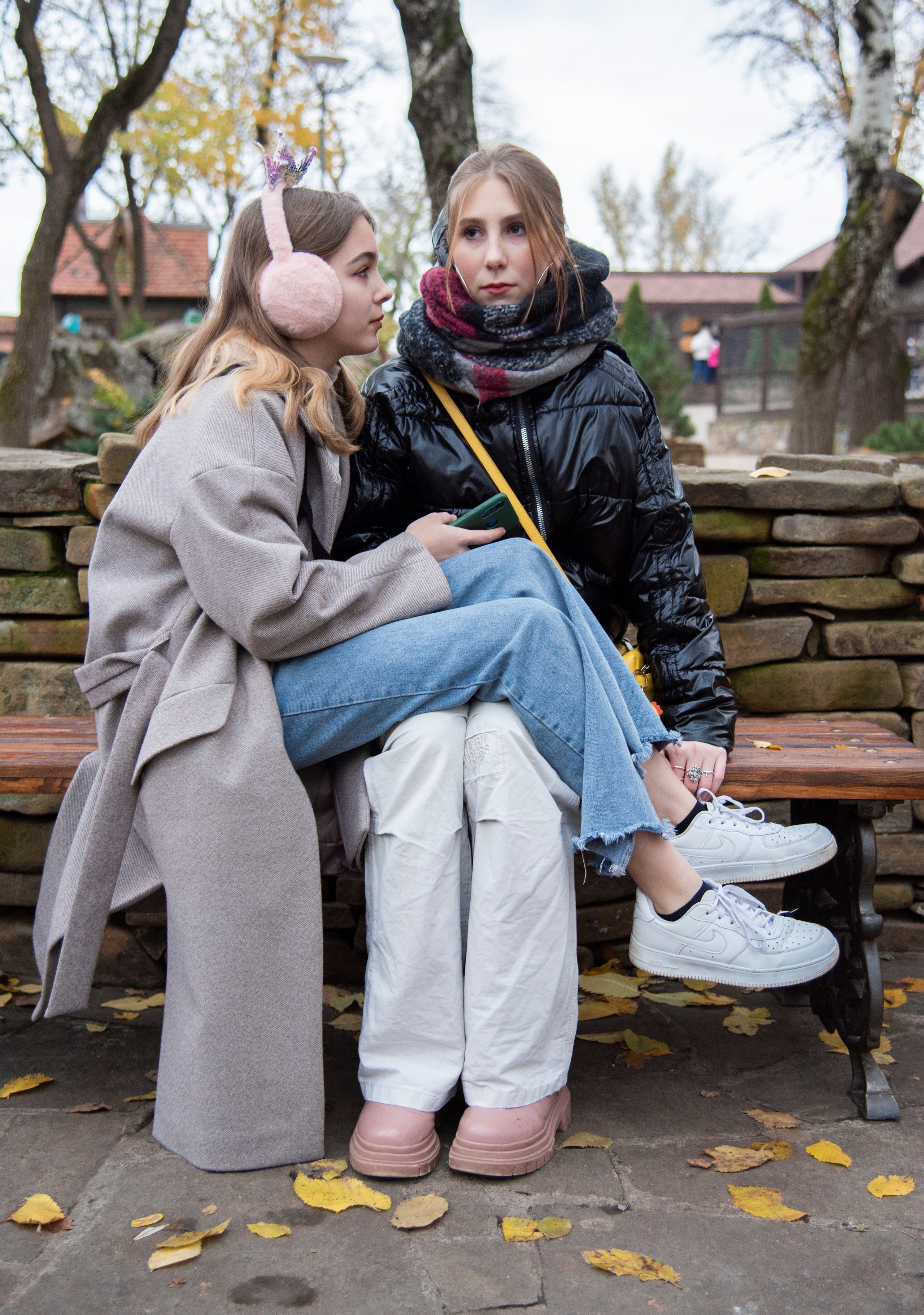 две девушки на лавочке, грустные. голубые джинсы. белые кроссовки. парк лога. осень