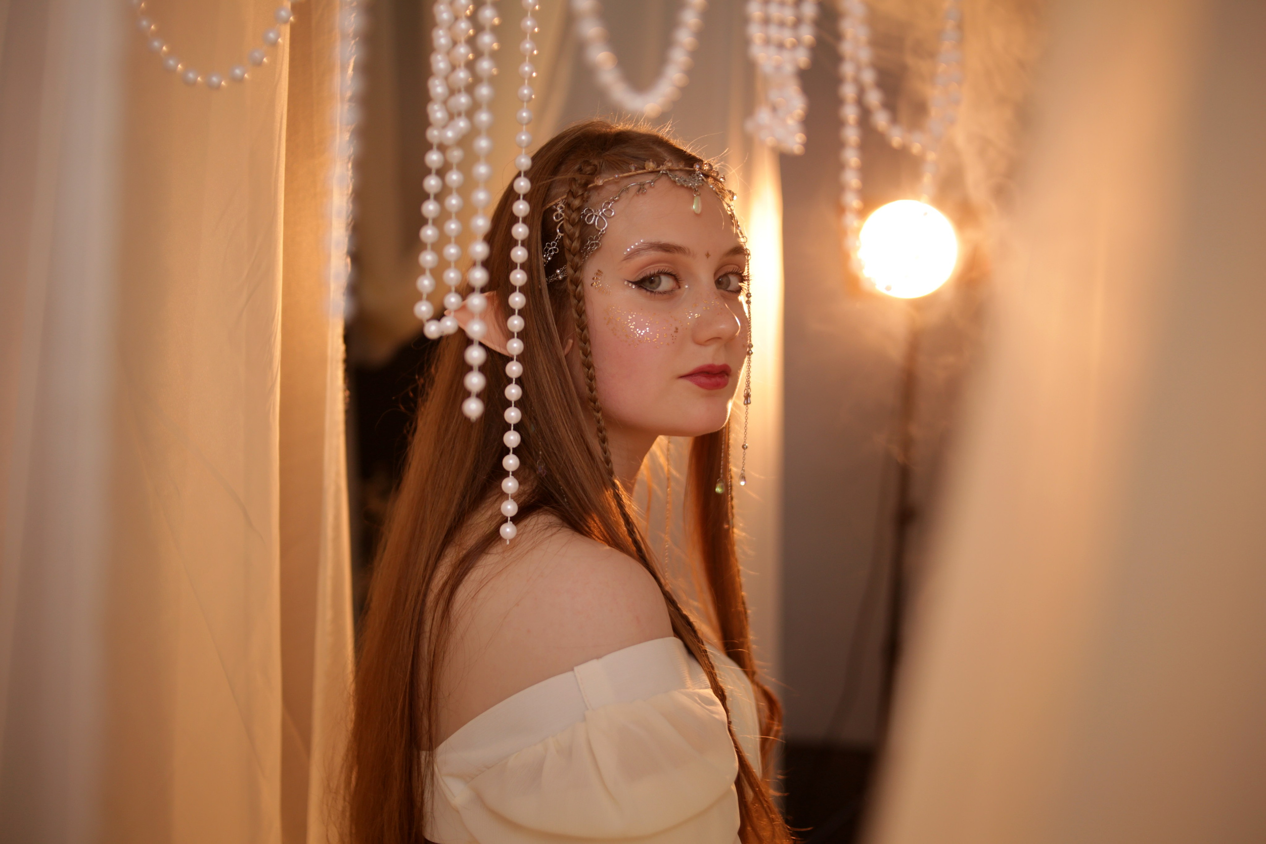 Тематическая фотосессия в Перми: девушка в белом платье с ушками и головным убором, сидит на кровати под полупрозрачным балдахином. Атмосферное освещение.