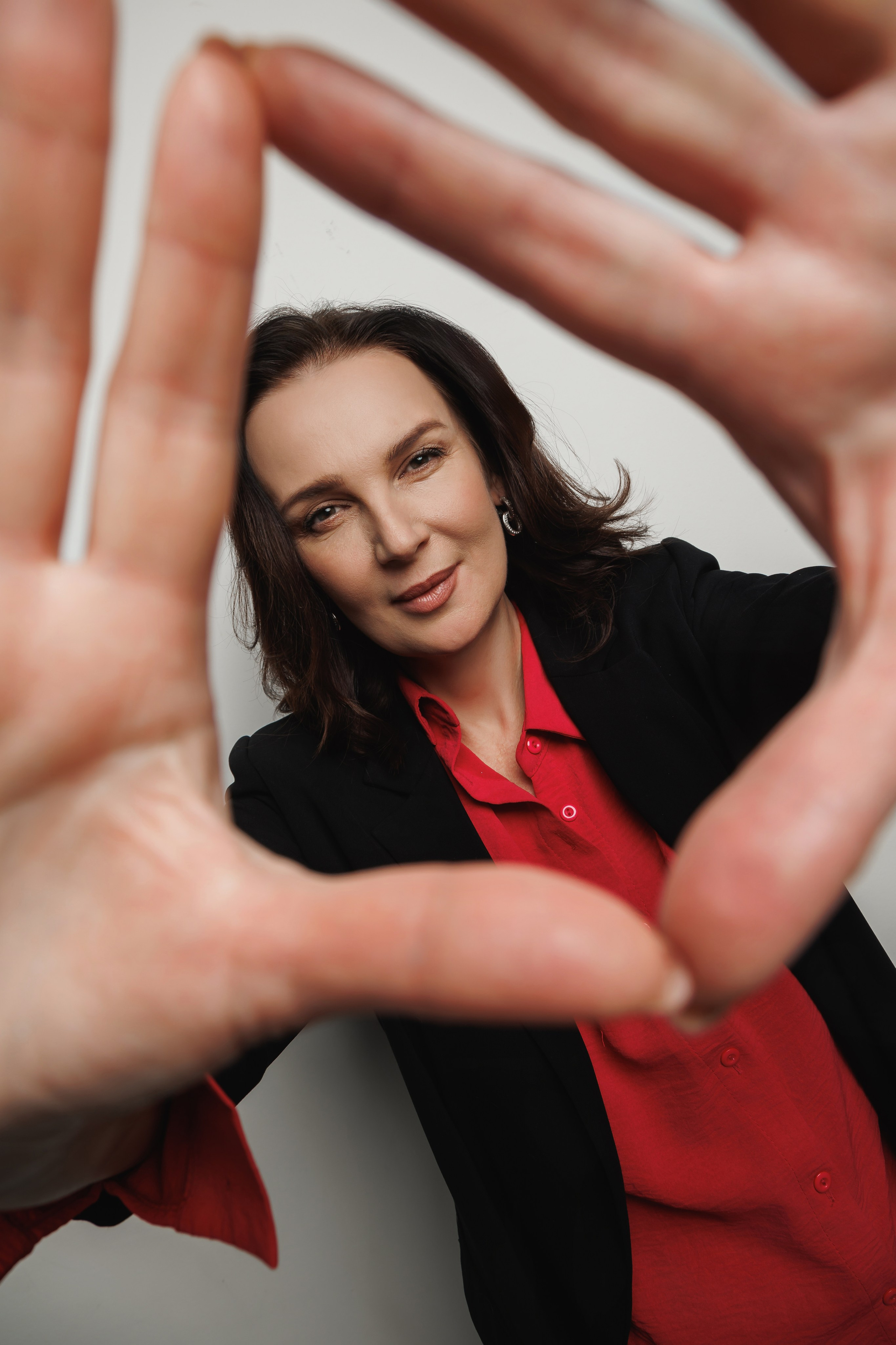 Креативный портрет: девушка-психолог складывает руки в пирамиду, через которую видно её задумчивое лицо. Нестандартная композиция.