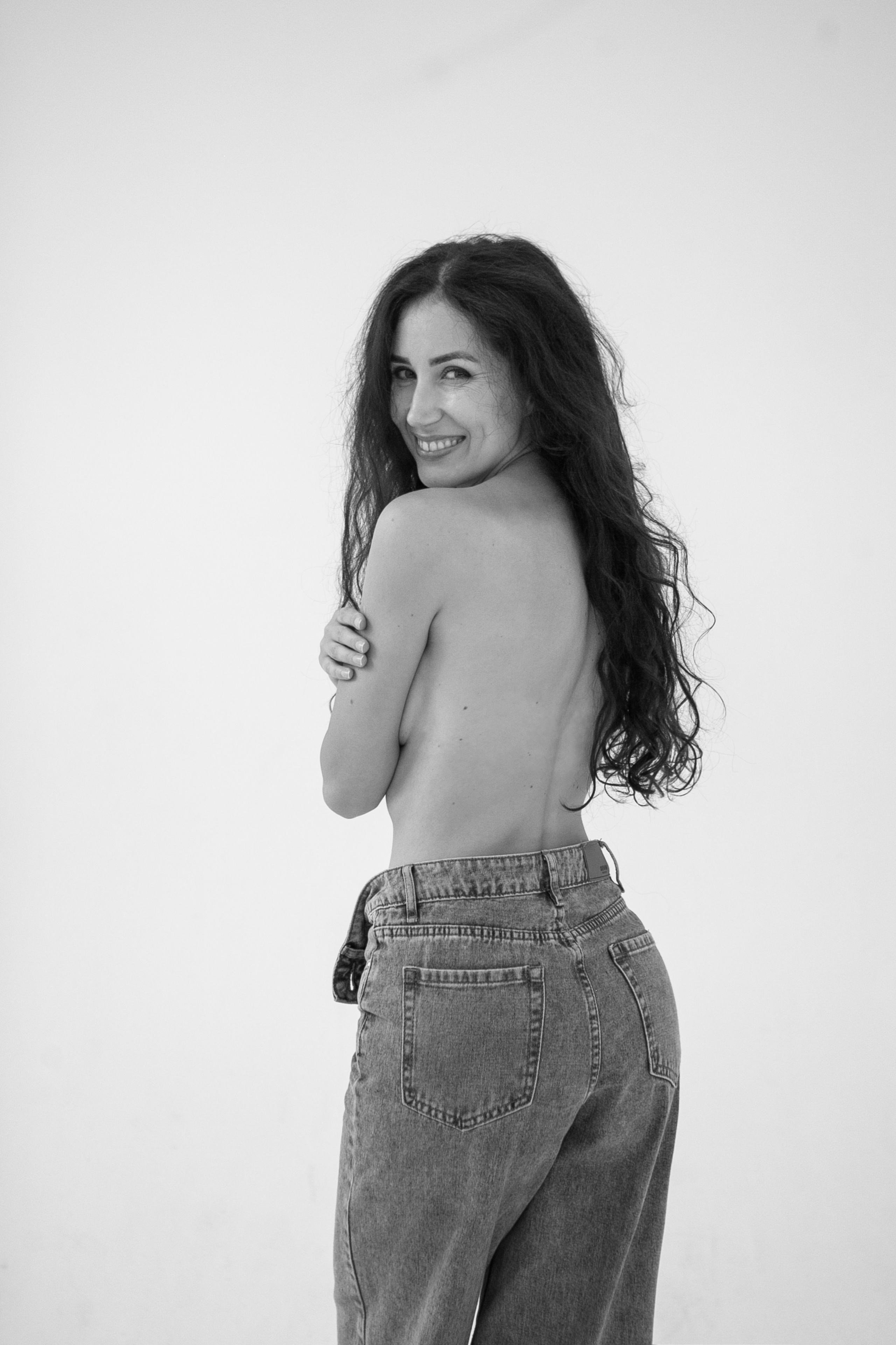 Девушка в джинсах топлес позирует на белом фоне