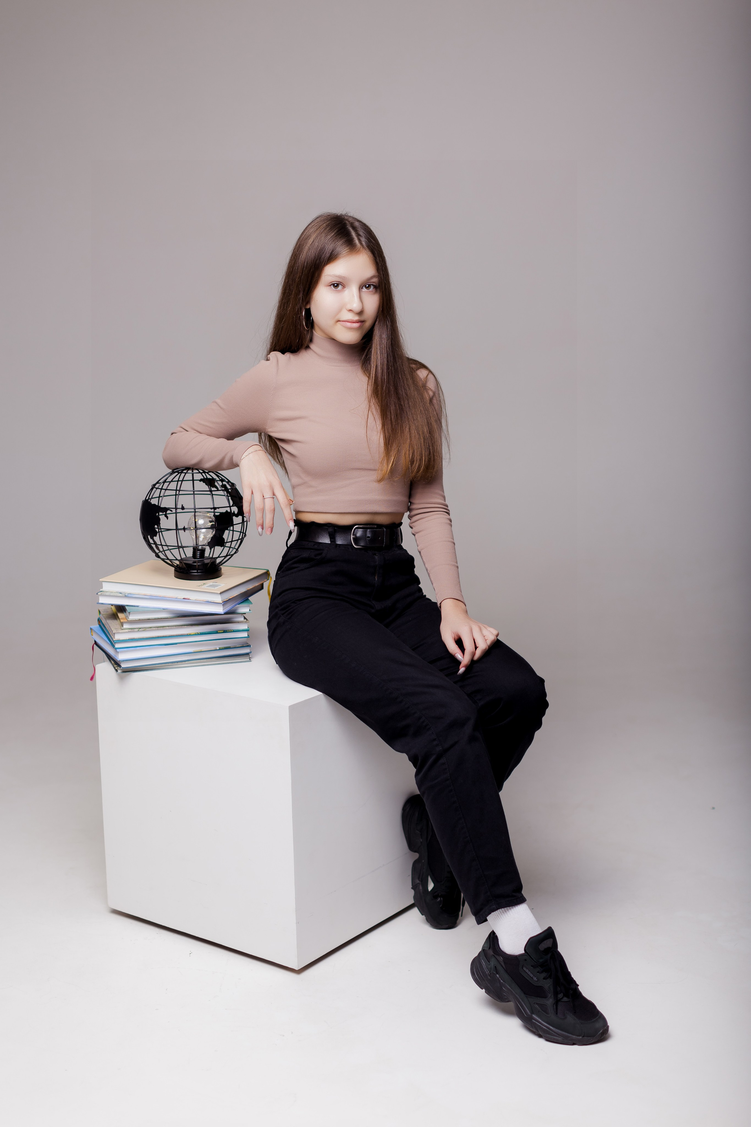 Девушка сидит на тумбе в фотостудии с глобусом