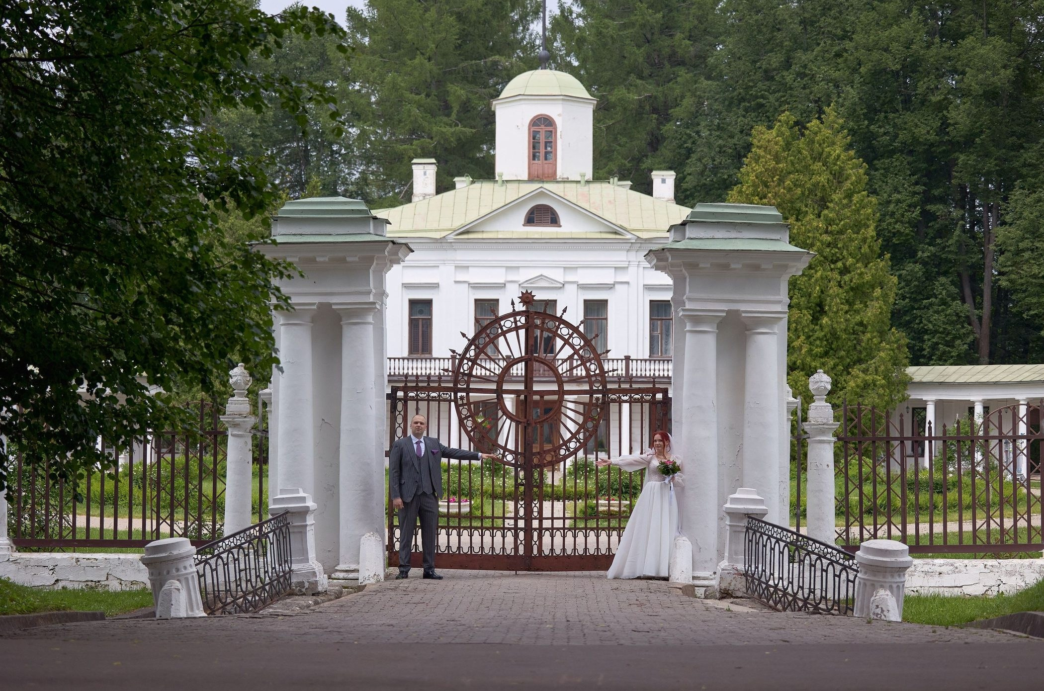 Невеста и жених у ворот позируют фотографу в Середняково
