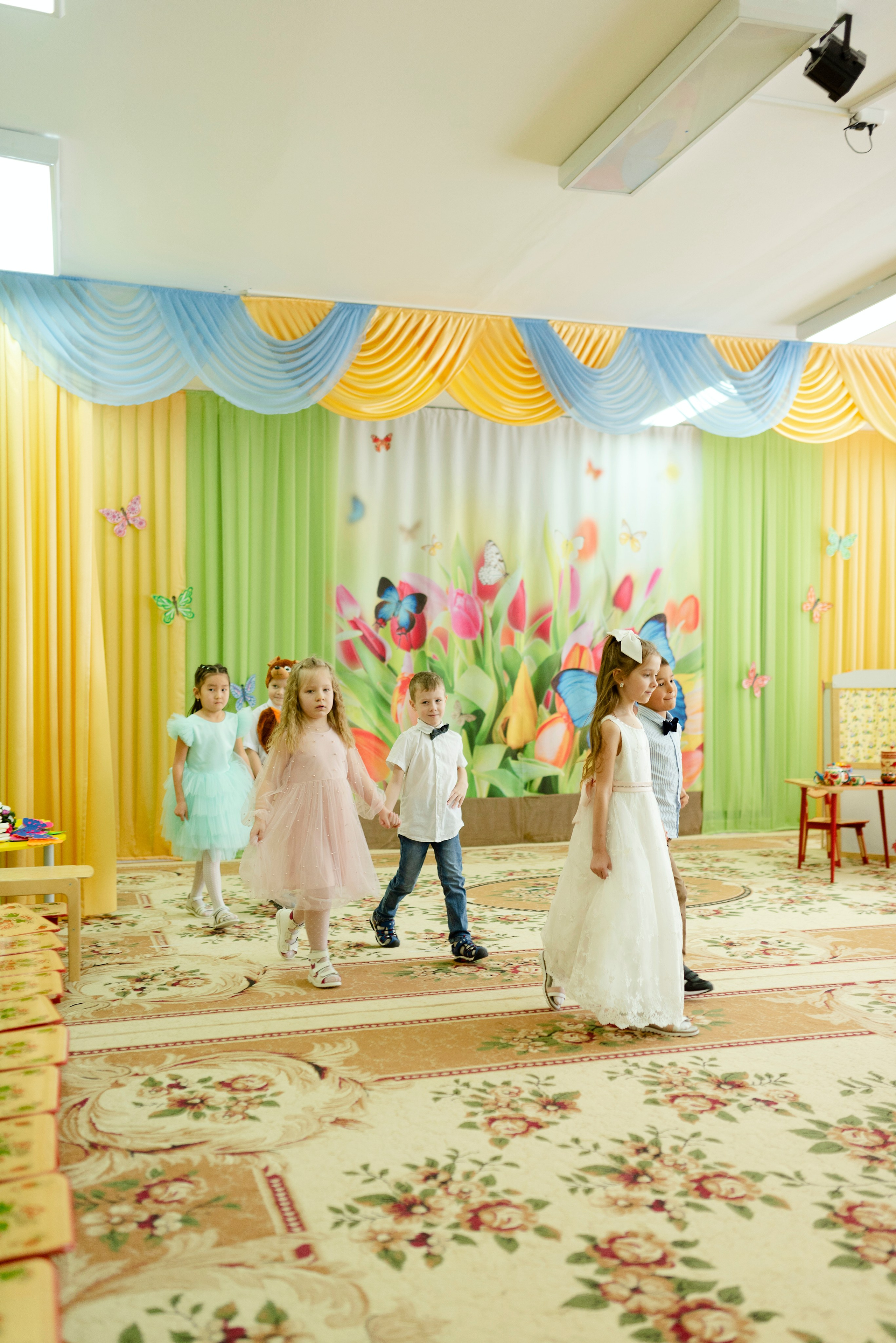 Дети танцуют веселый танец в праздничных костюмах на утреннике 8 марта в детском саду.