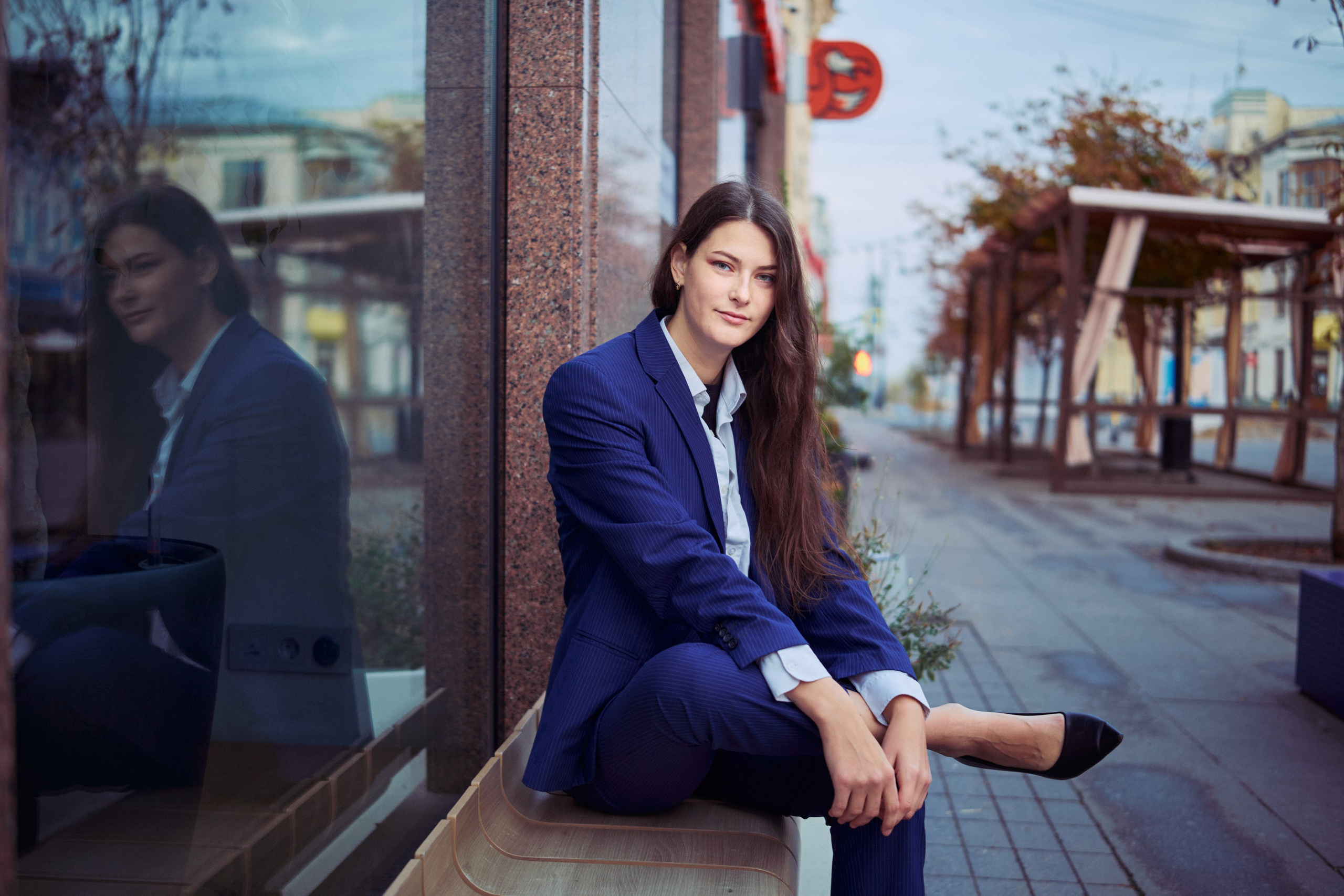 Женщина в белой рубашке с лёгким небрежным стилем, сидящая в городской среде