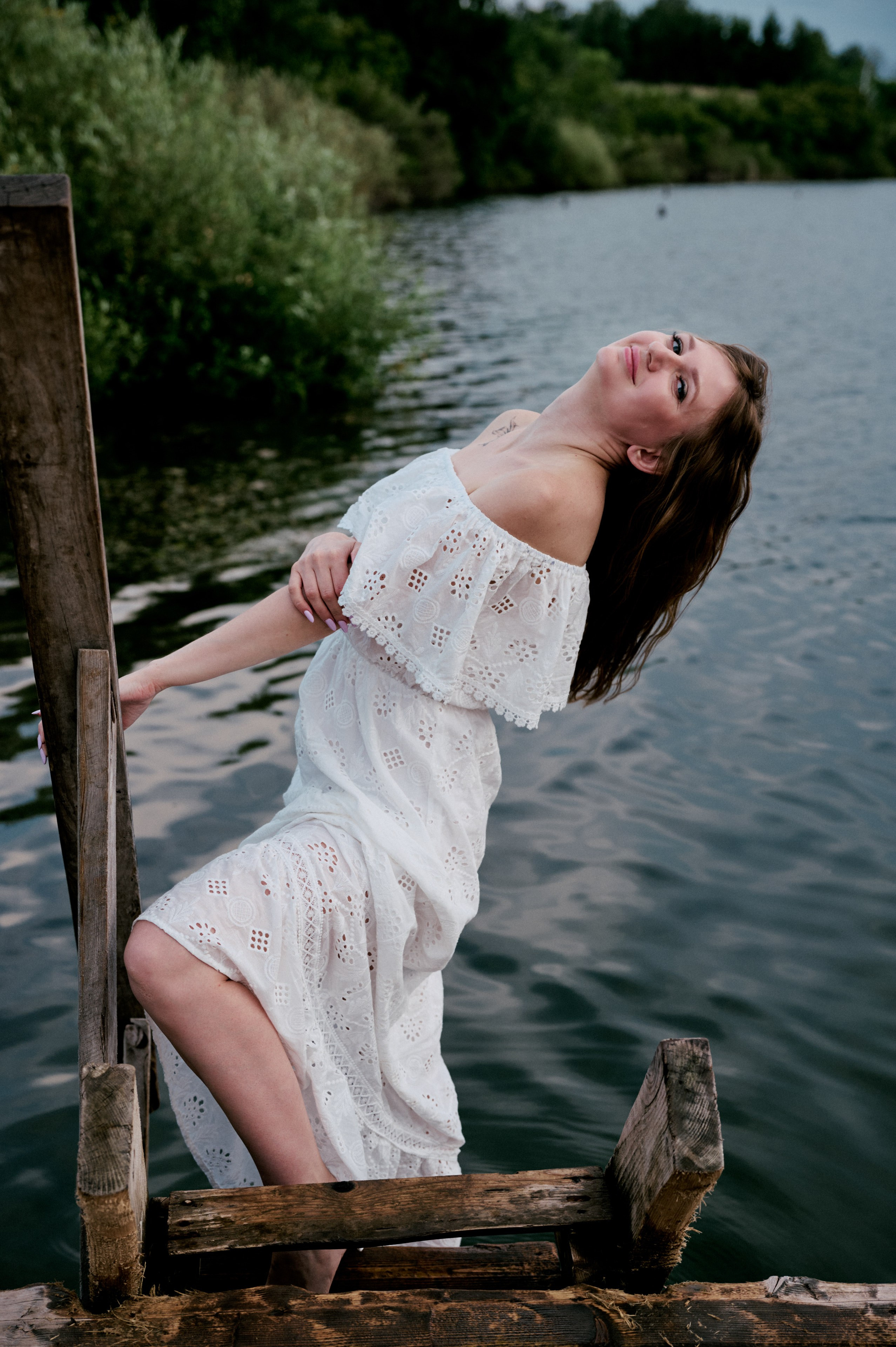 Евгения стоит на деревянном пирсе в белом платье.