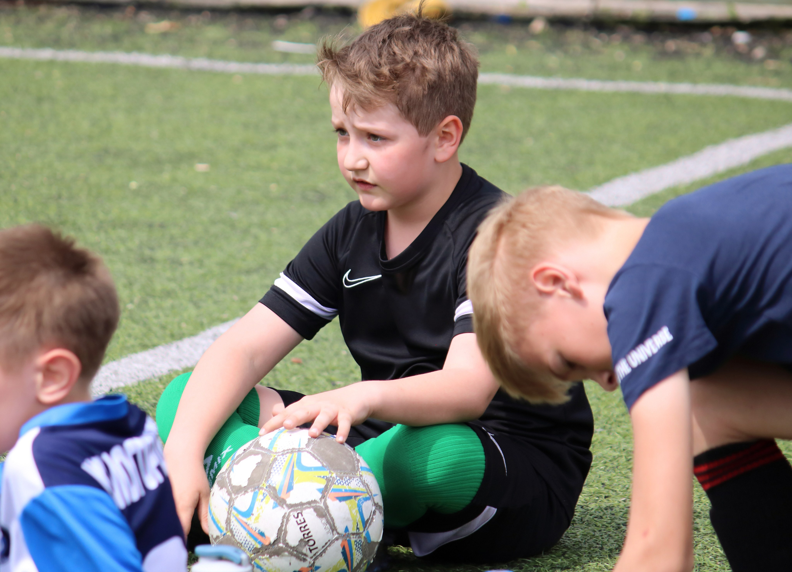 Юный футболист с мячом сидит на траве стадиона