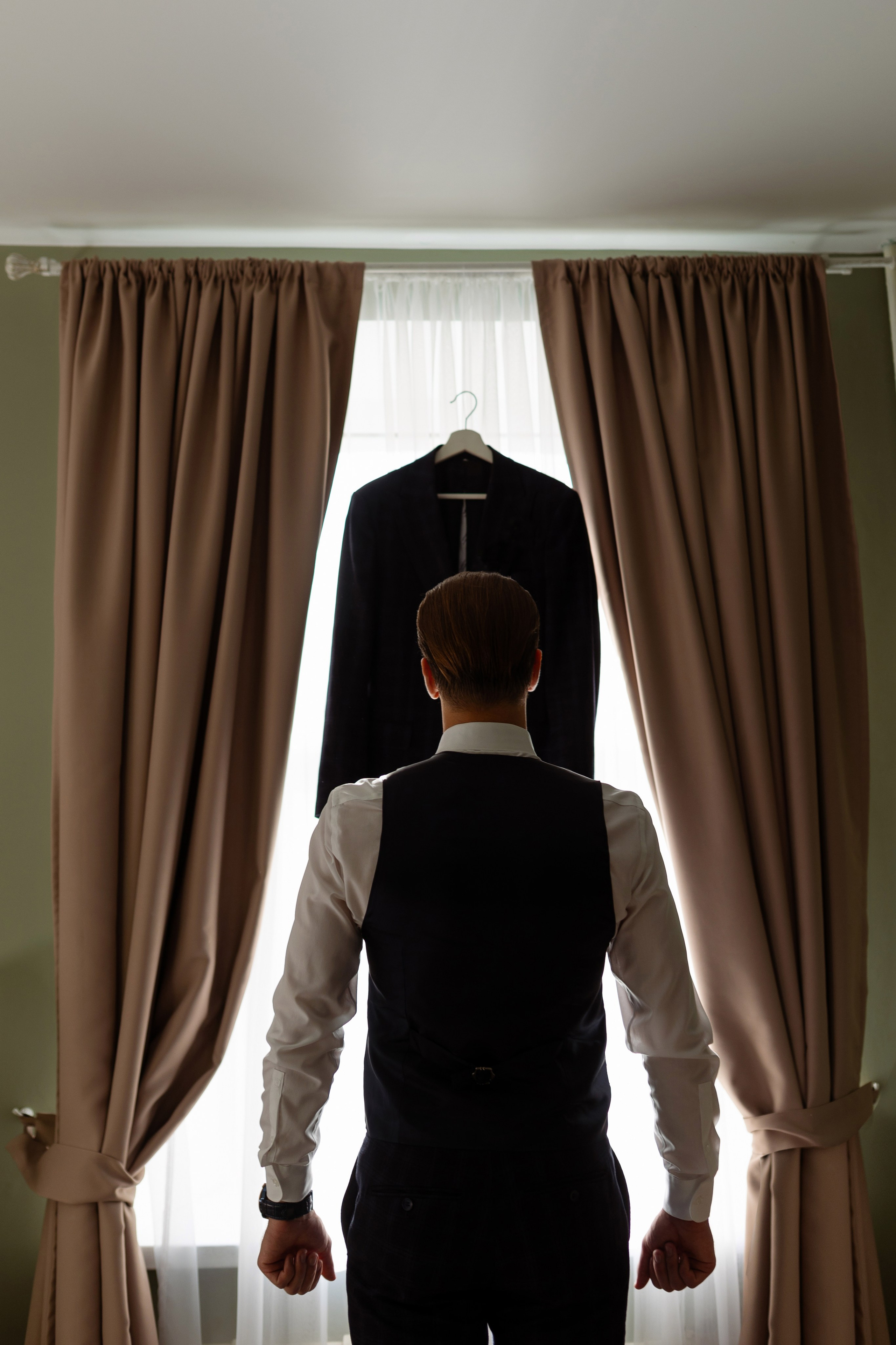 Жених стоит у окна спиной к оБъективу.