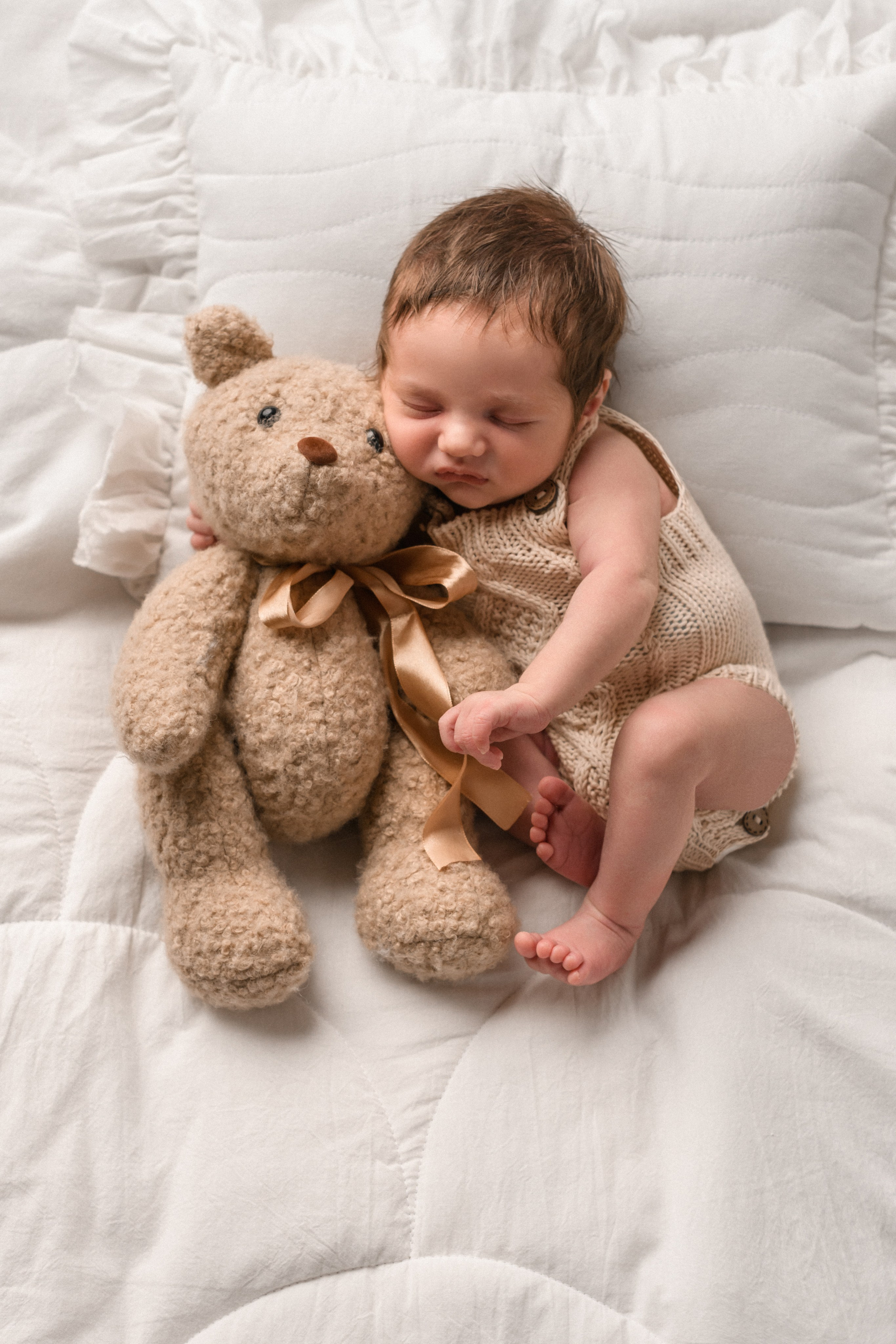Новорожденный мальчик лежит на уютной подушке и обнимает плюшевого медведя в детской фотостудии Алёны Лариной "В капусте"