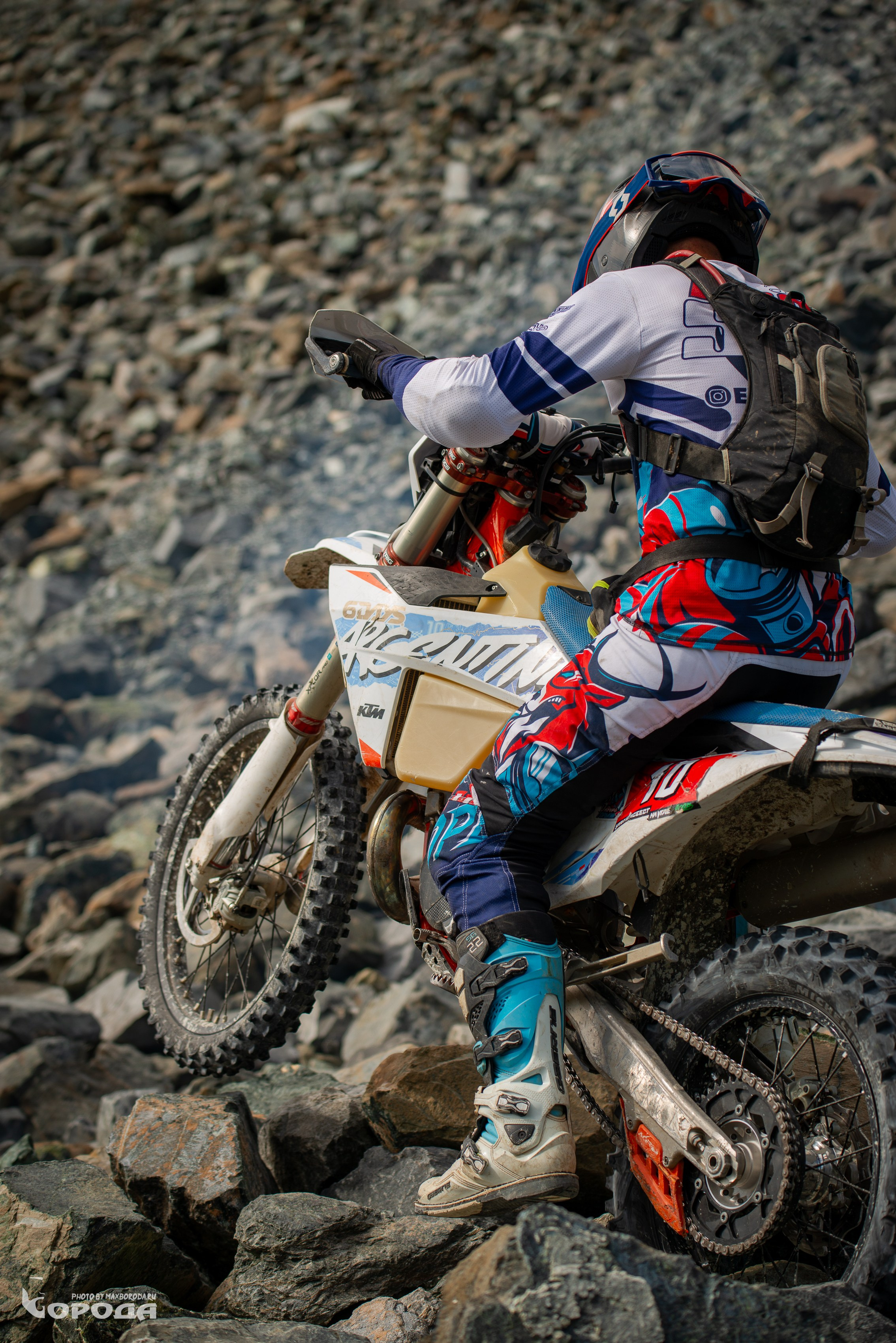 Гонщик на эндуро маневрирует среди камней, экипировка с красно-синим узором