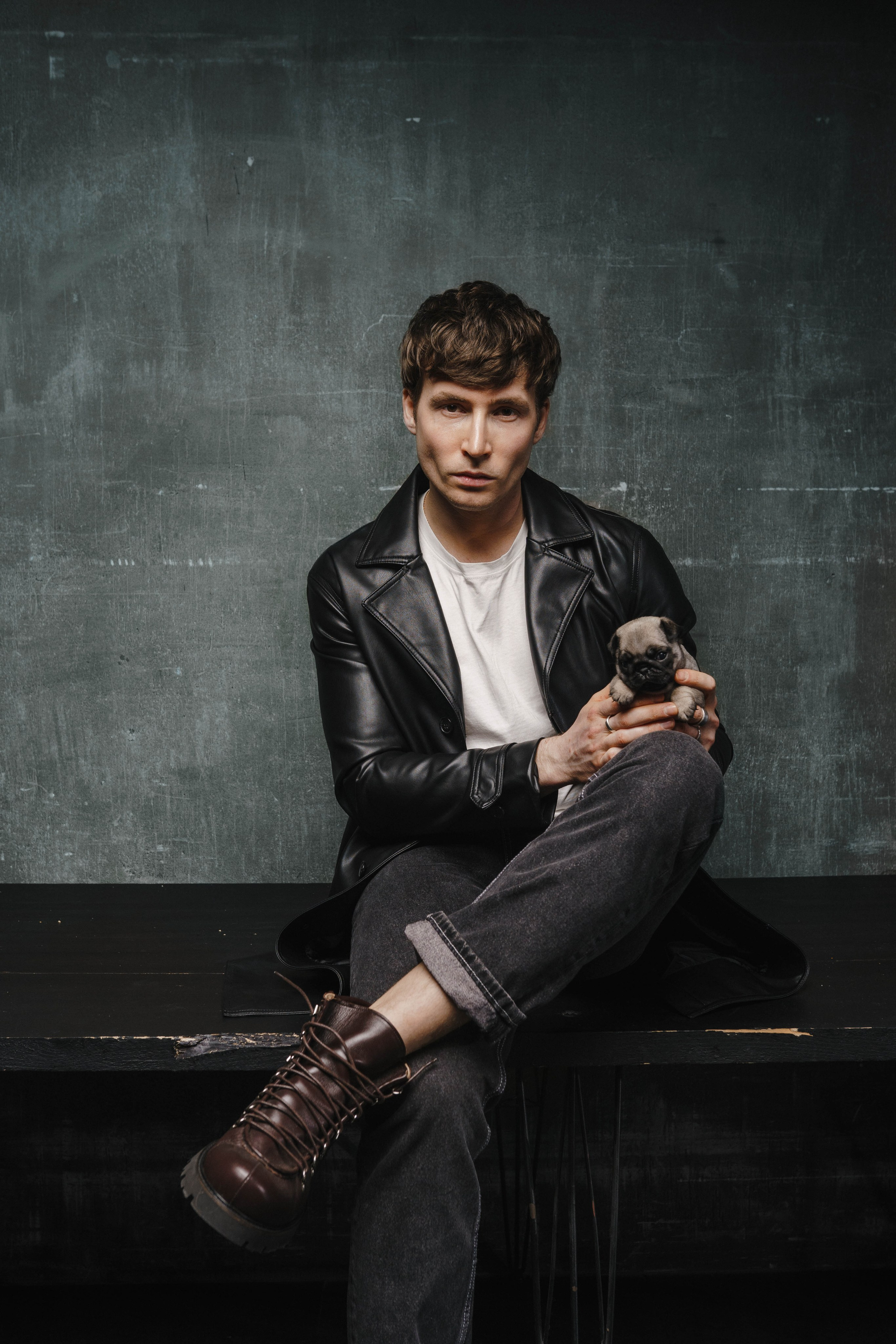 Брутальный мужчина в кожаной куртке бережно держит щенка на ладони.