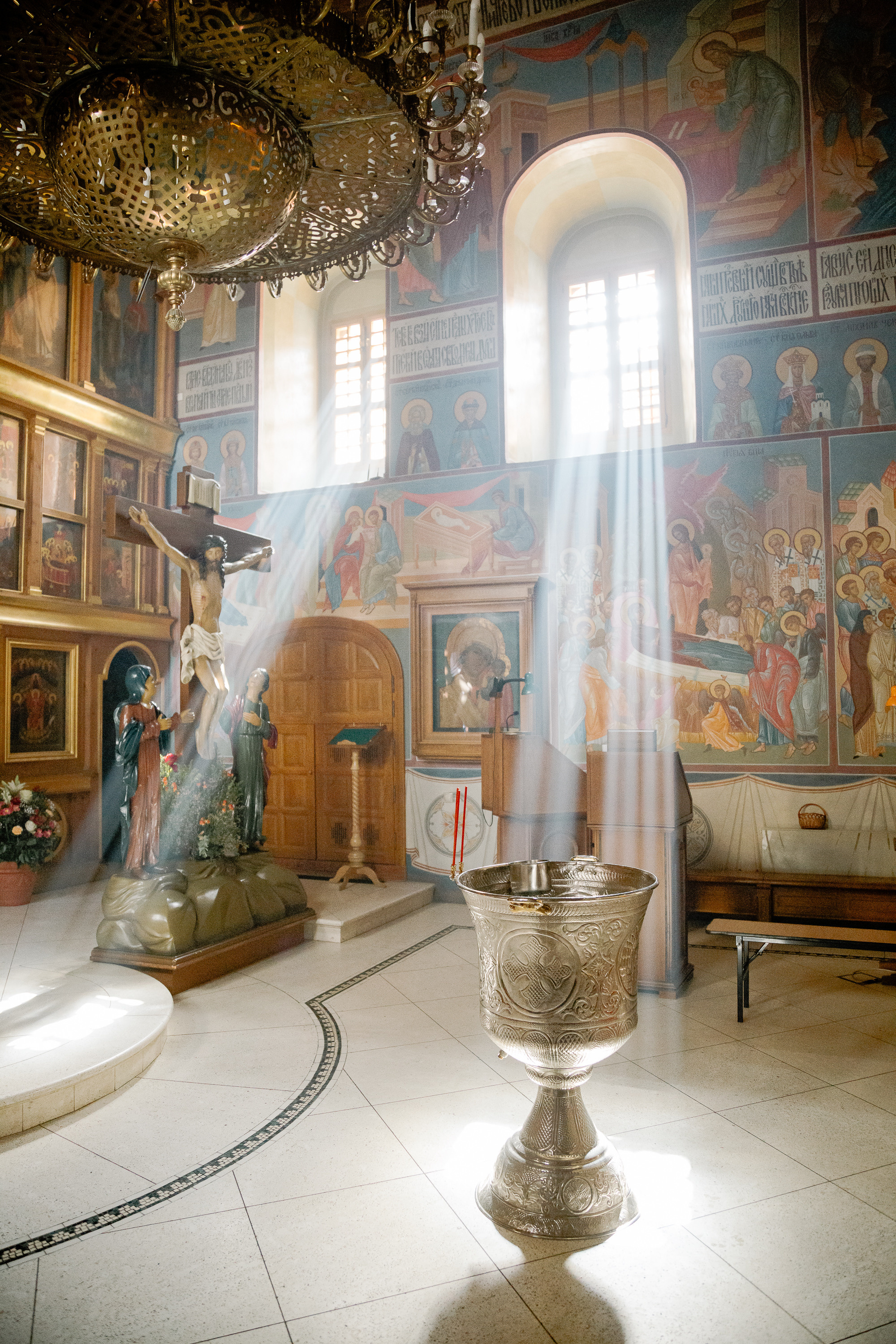 Крестильная купель стоит в храме и на нее падают лучи солнца из окна.