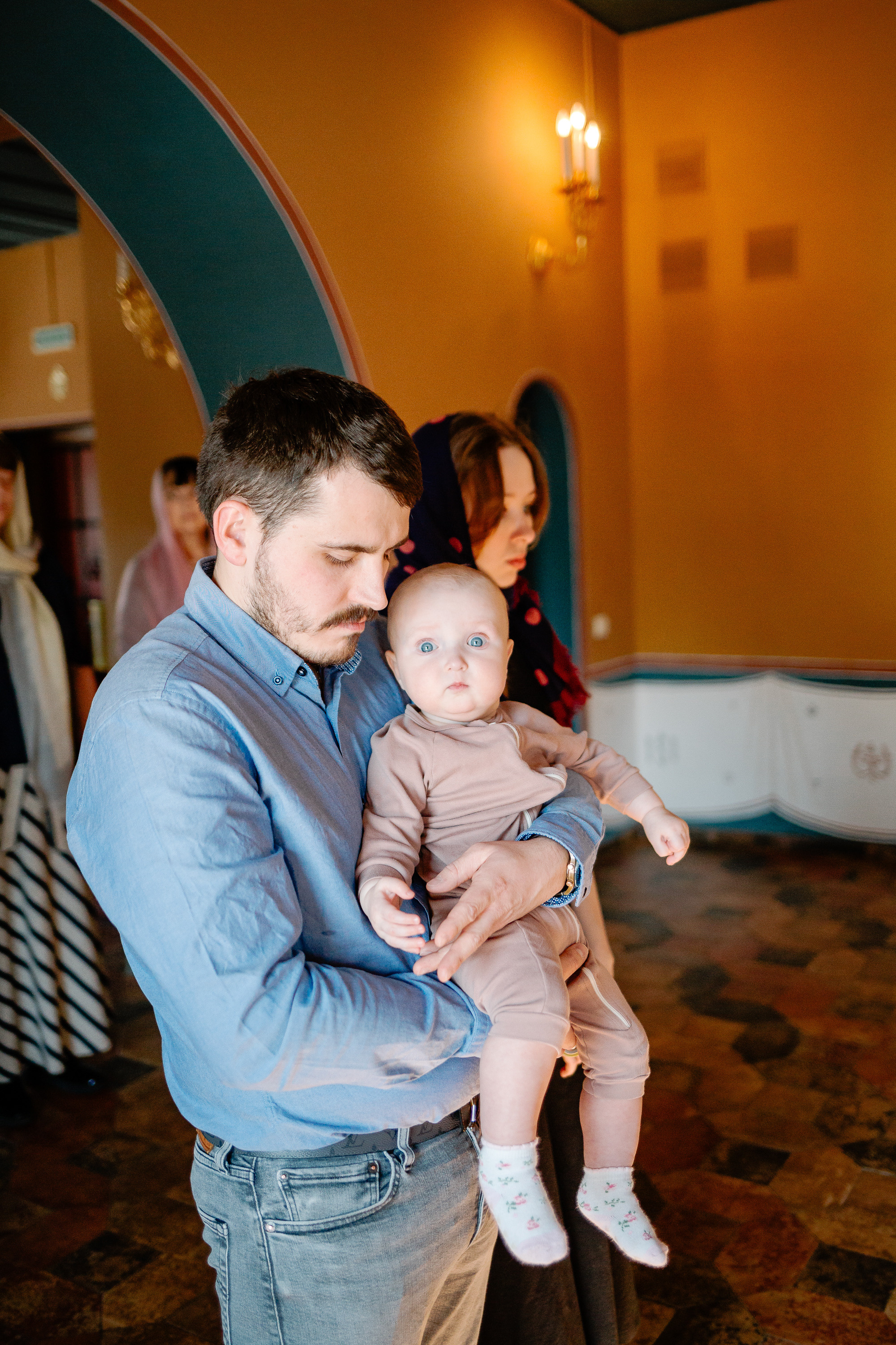 Крещение младенца. Крестный в храме держит на руках маленького ребенка.