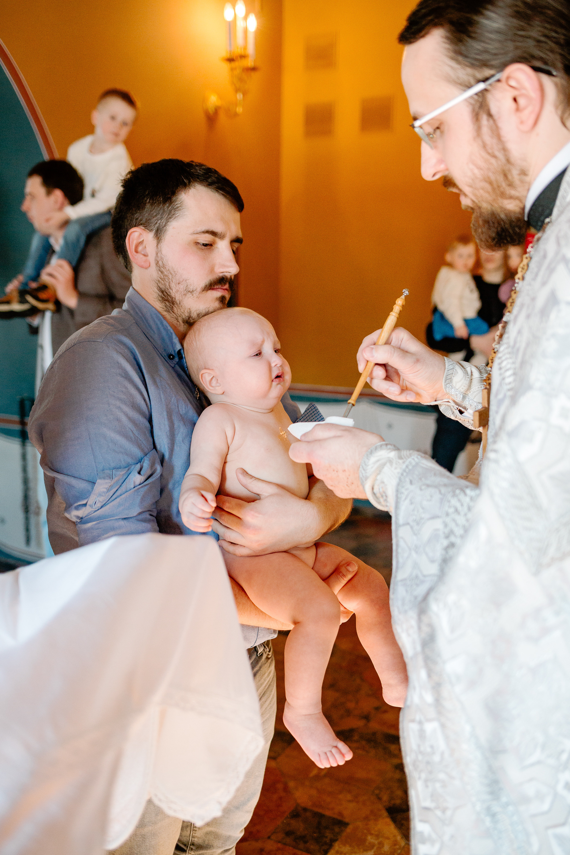 Крестный держит на руках маленького ребенка. Батюшка крестит малыша.