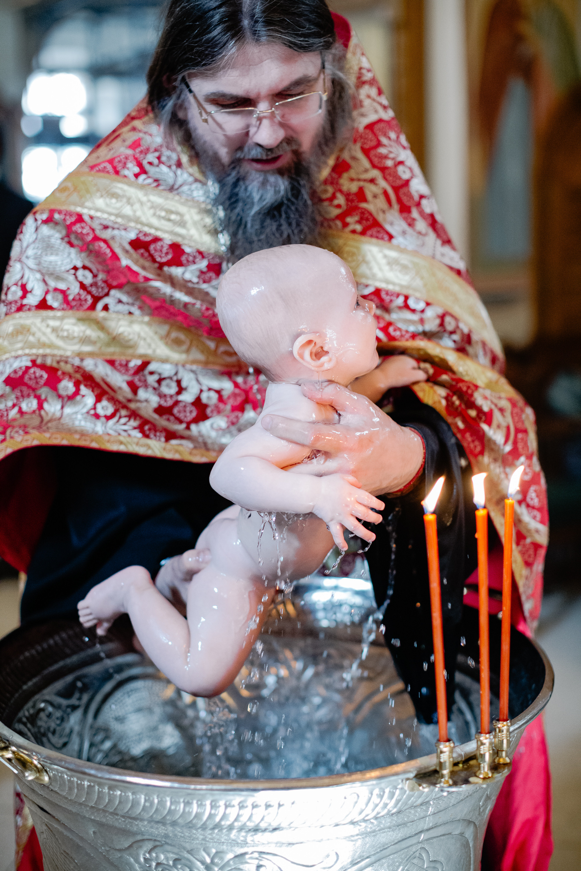 Батюшка окунает в купель младенца, чтобы покрестить его.