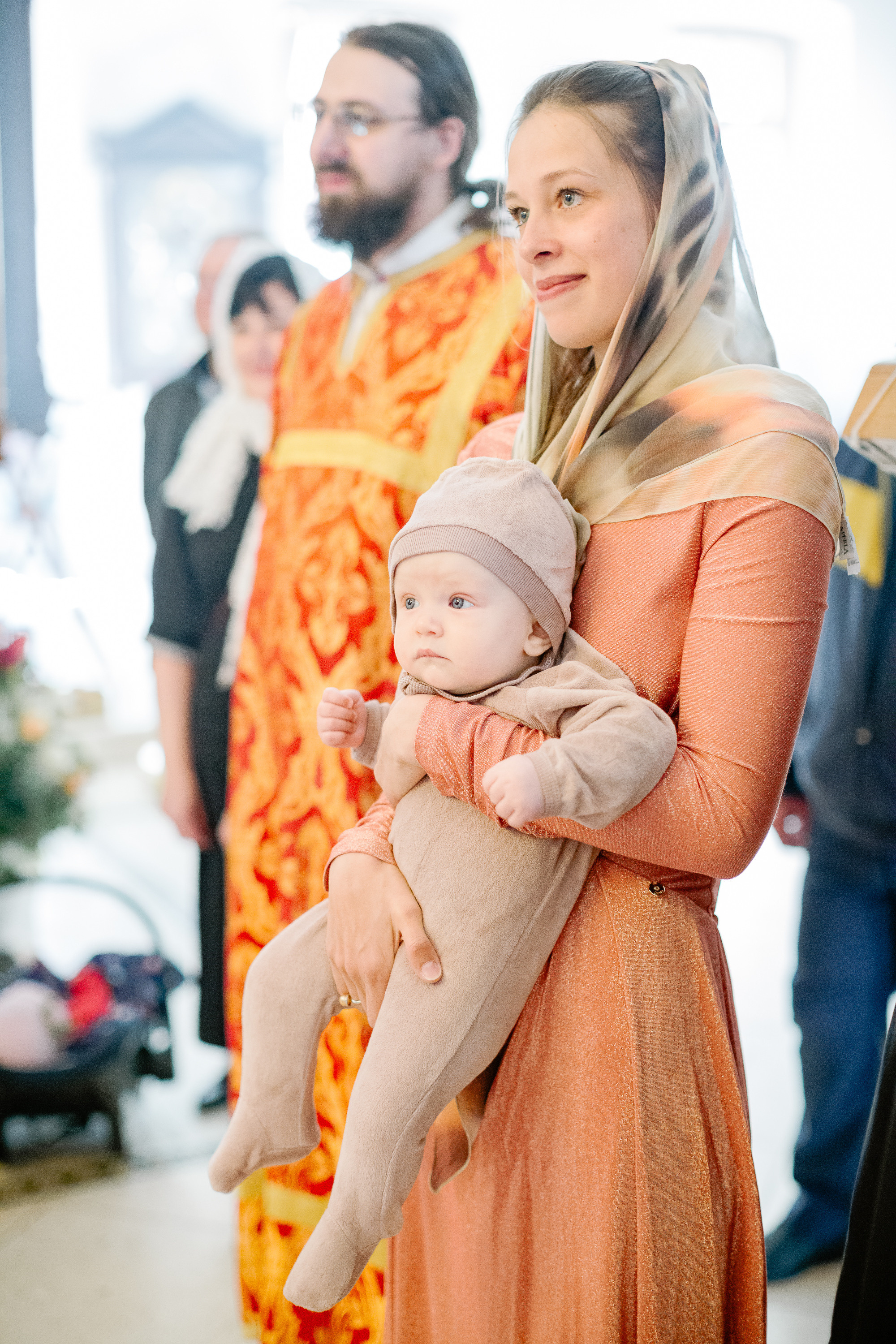 Мать в храме держит на руках младенца, которого будут крестить. 