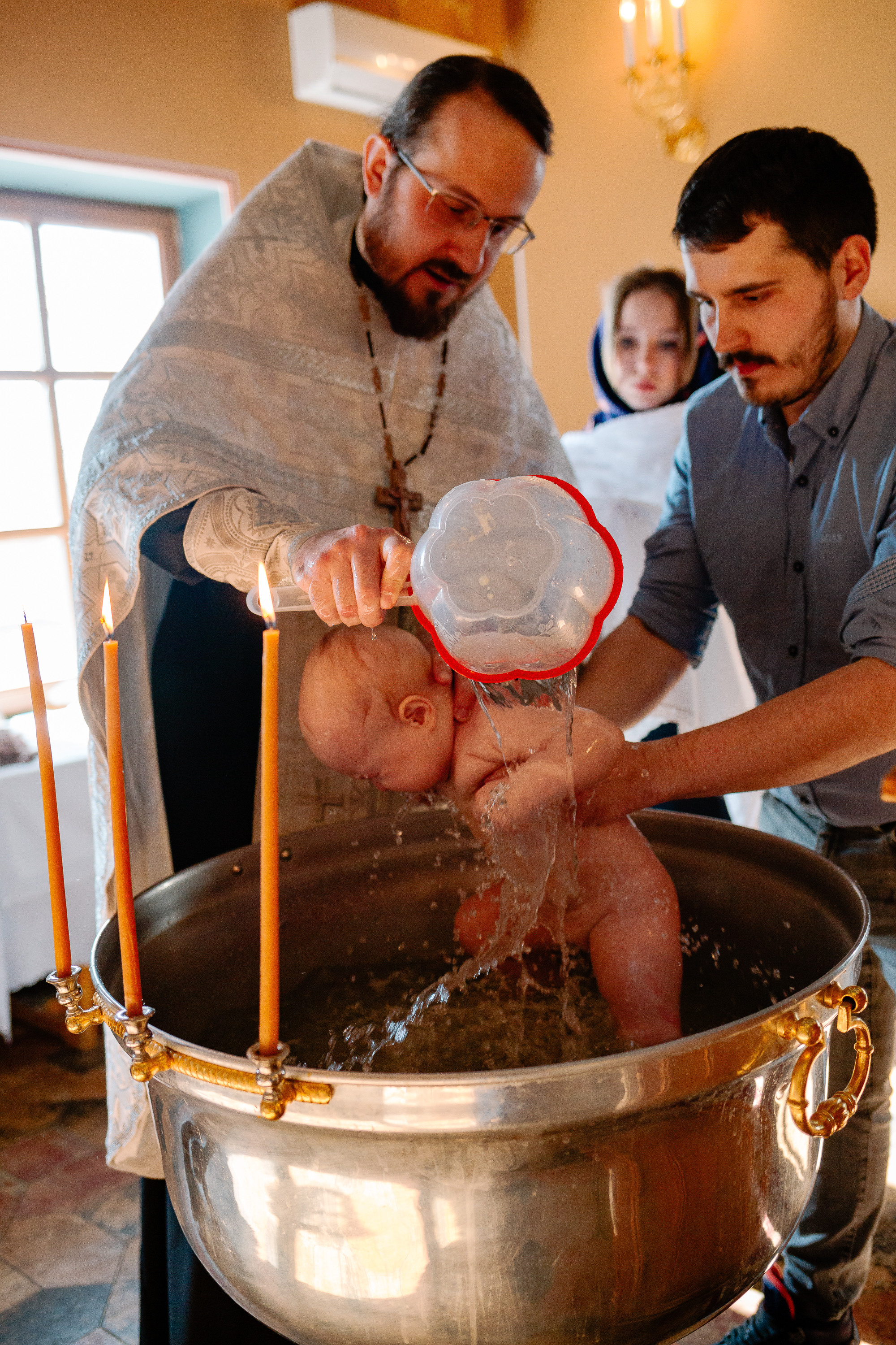 Батюшка окунает в купель младенца.