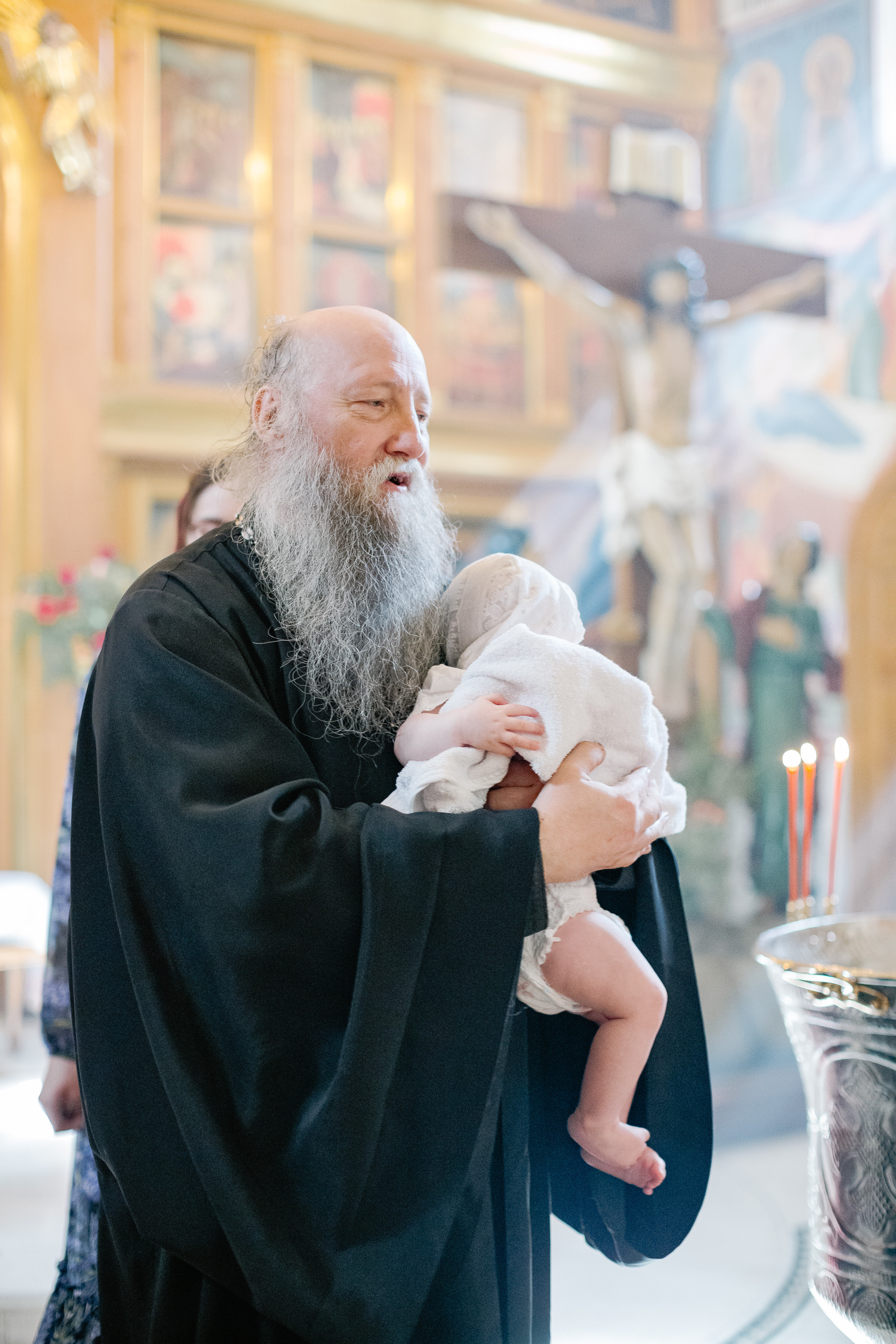 Крестный батюшка идет с младенцем на руках по храму во время крещения.