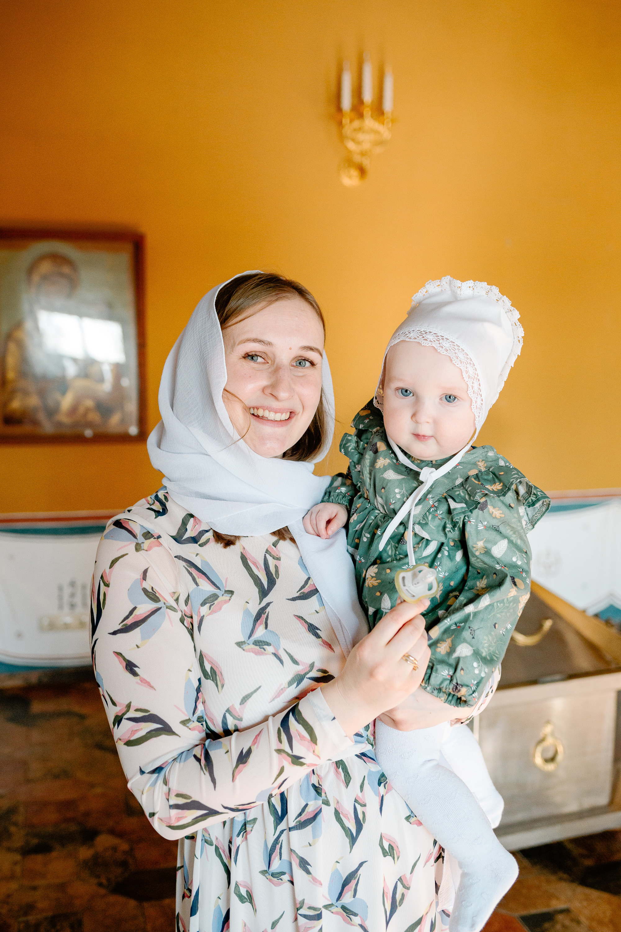 Ребенок после крещения сидит на руках у мамы в храме и светит солнце.