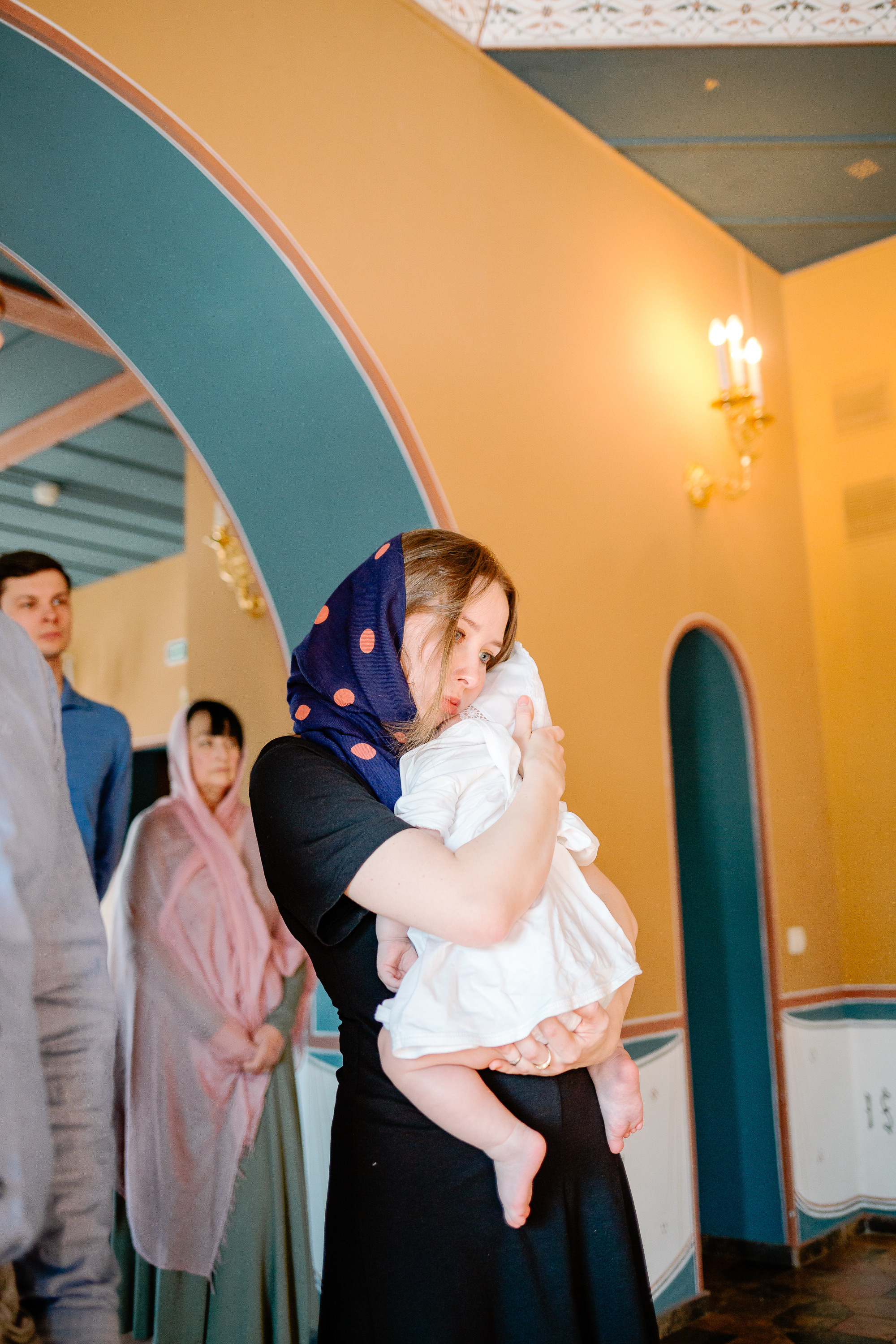 Крестная прижимает к себе маленького ребенка в храме.