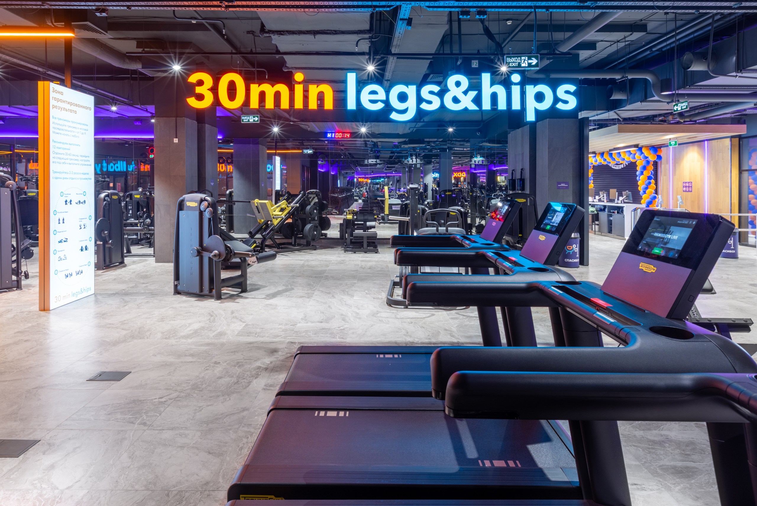 Большая неоновая надпись legs and hips в фитнес зале. Беговая дорожка в стильном тренажёрном клубе.