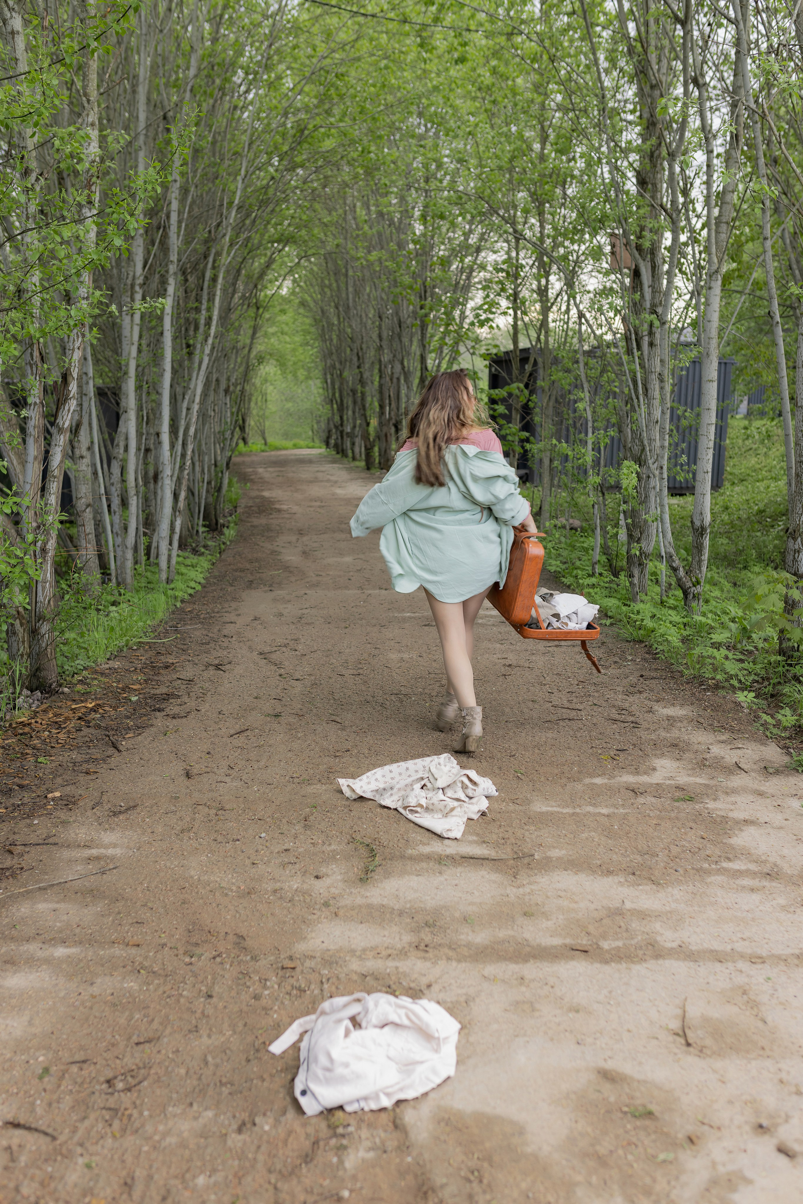 Девушка идет по дороге с чемоданом в руке, из него вываливается одежда