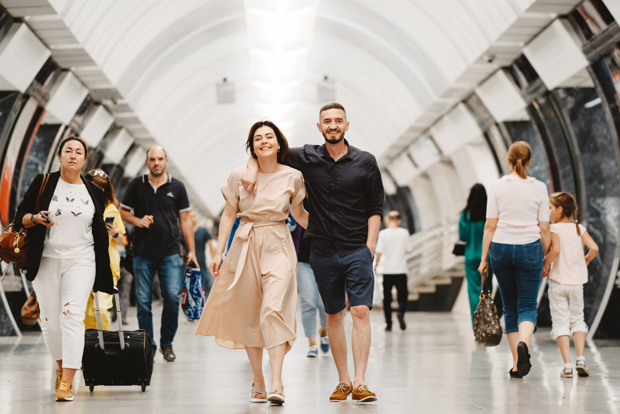 Только что поженившиеся идут по метро.