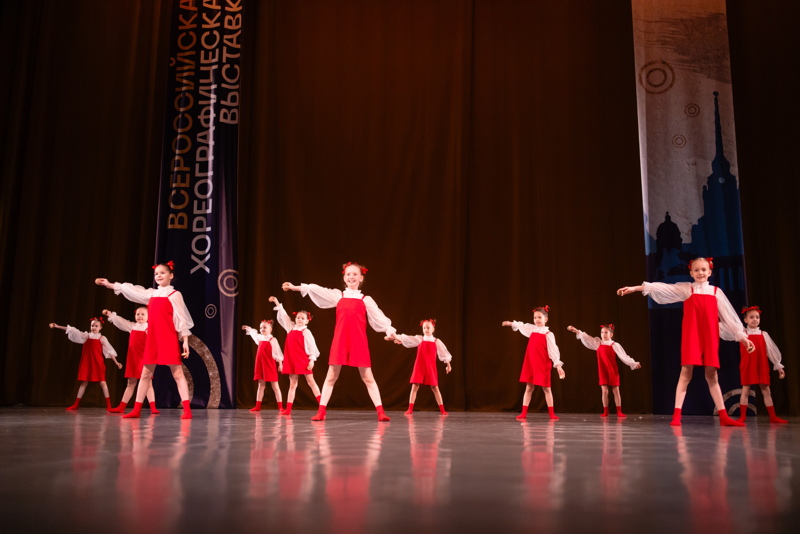 Широкий кадр сцены, где движение начинается с одного угла и расходится по всем артистам.