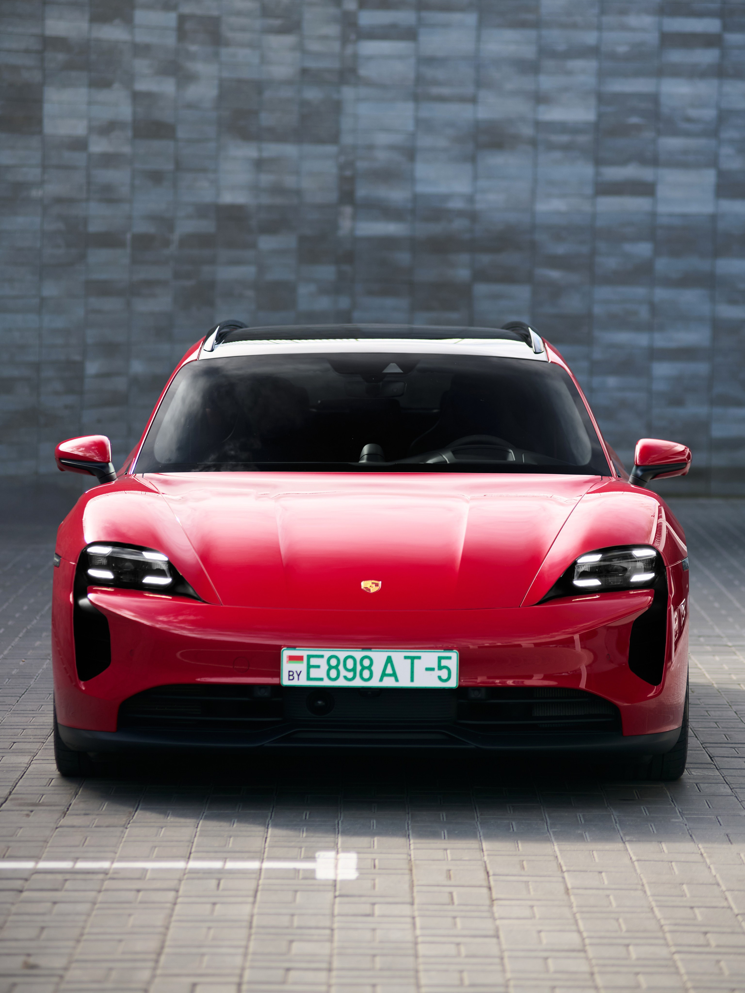 Красный Porsche Taycan GTS спереди на фоне серой стены