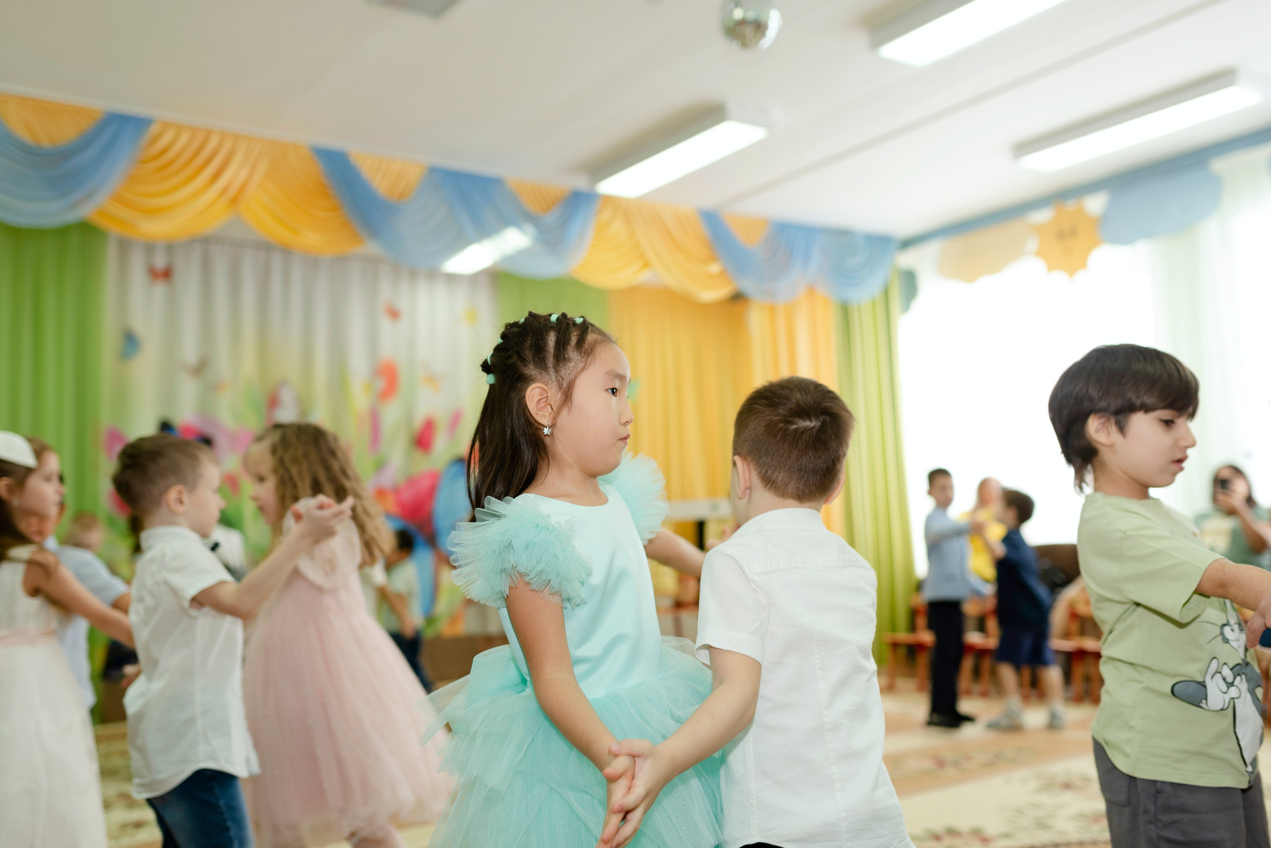 Дети танцуют веселый танец в праздничных костюмах на утреннике 8 марта в детском саду.