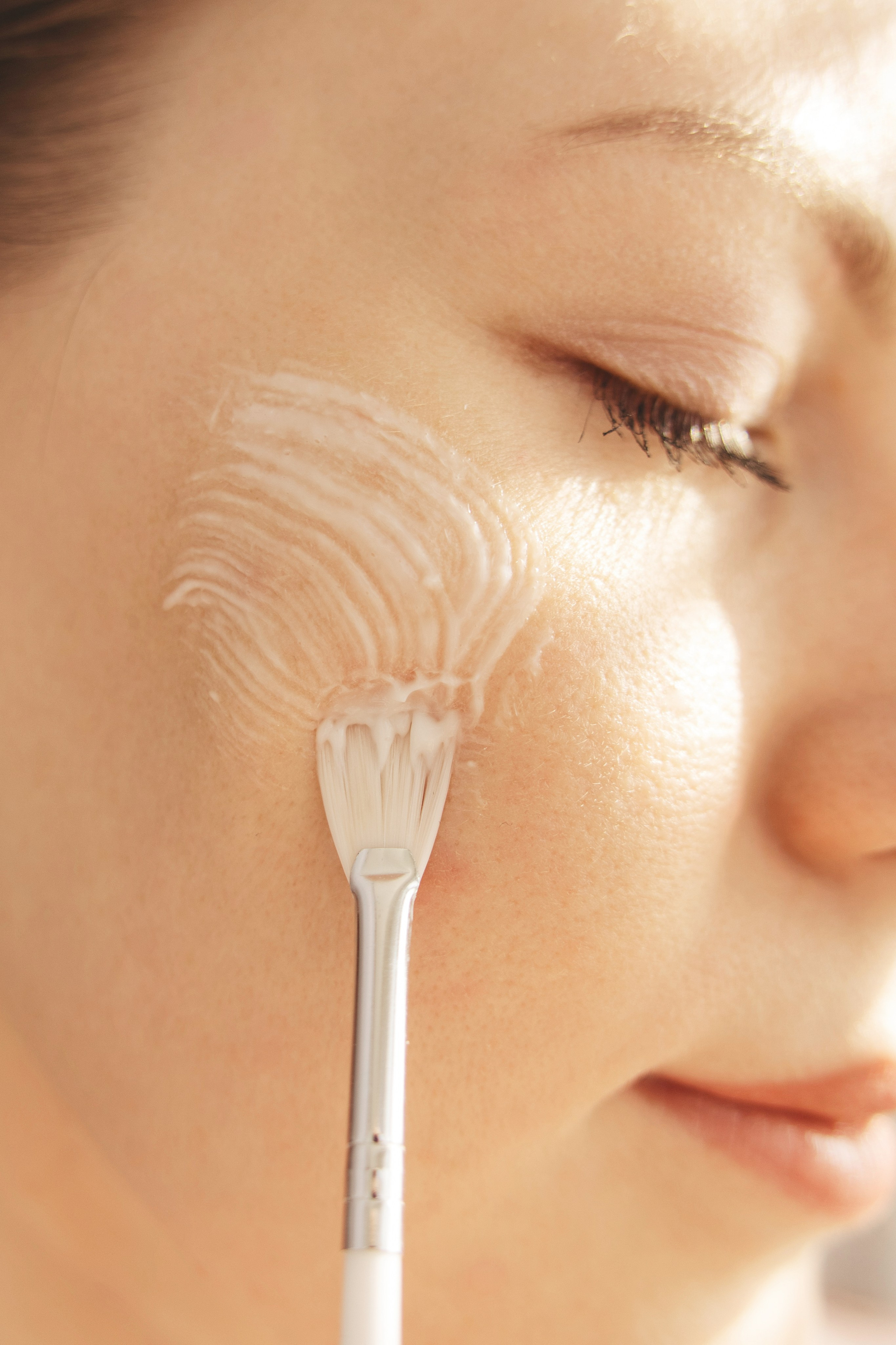 Косметолог наносит кисточкой крем на лицо