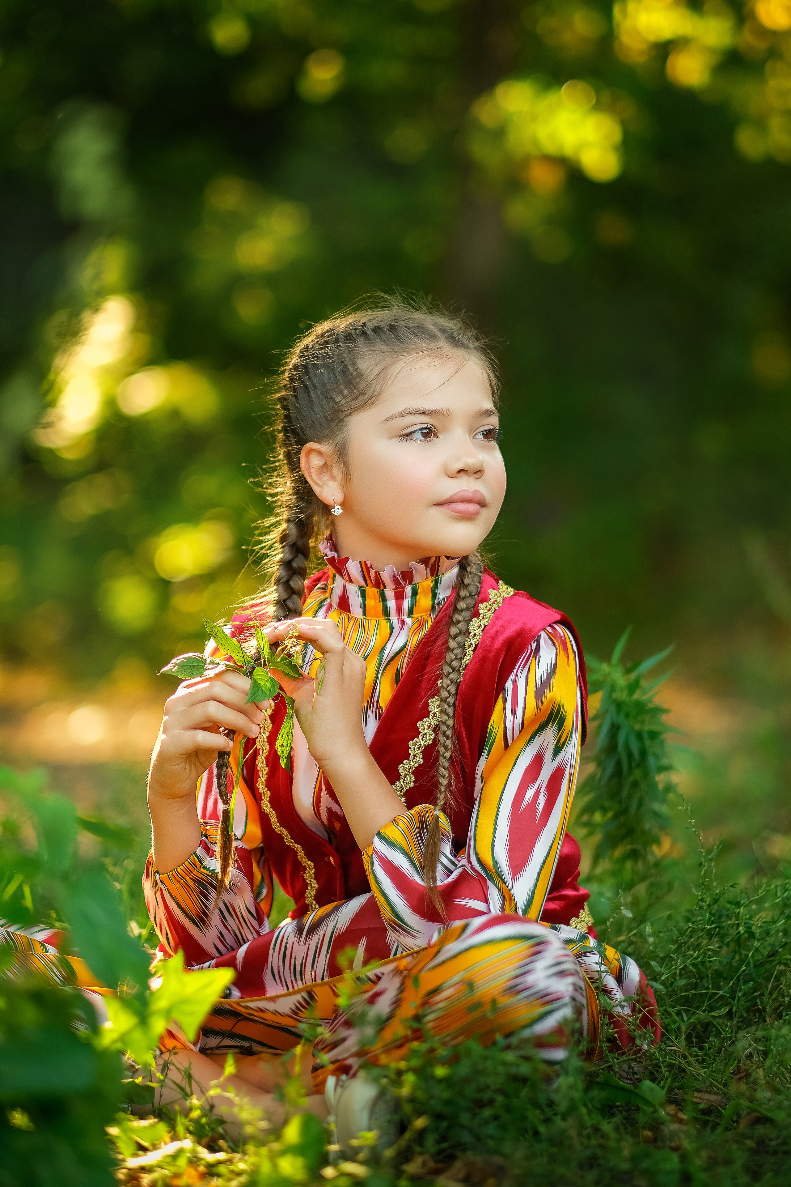 Девочка в национальном костюме сидит на поляне