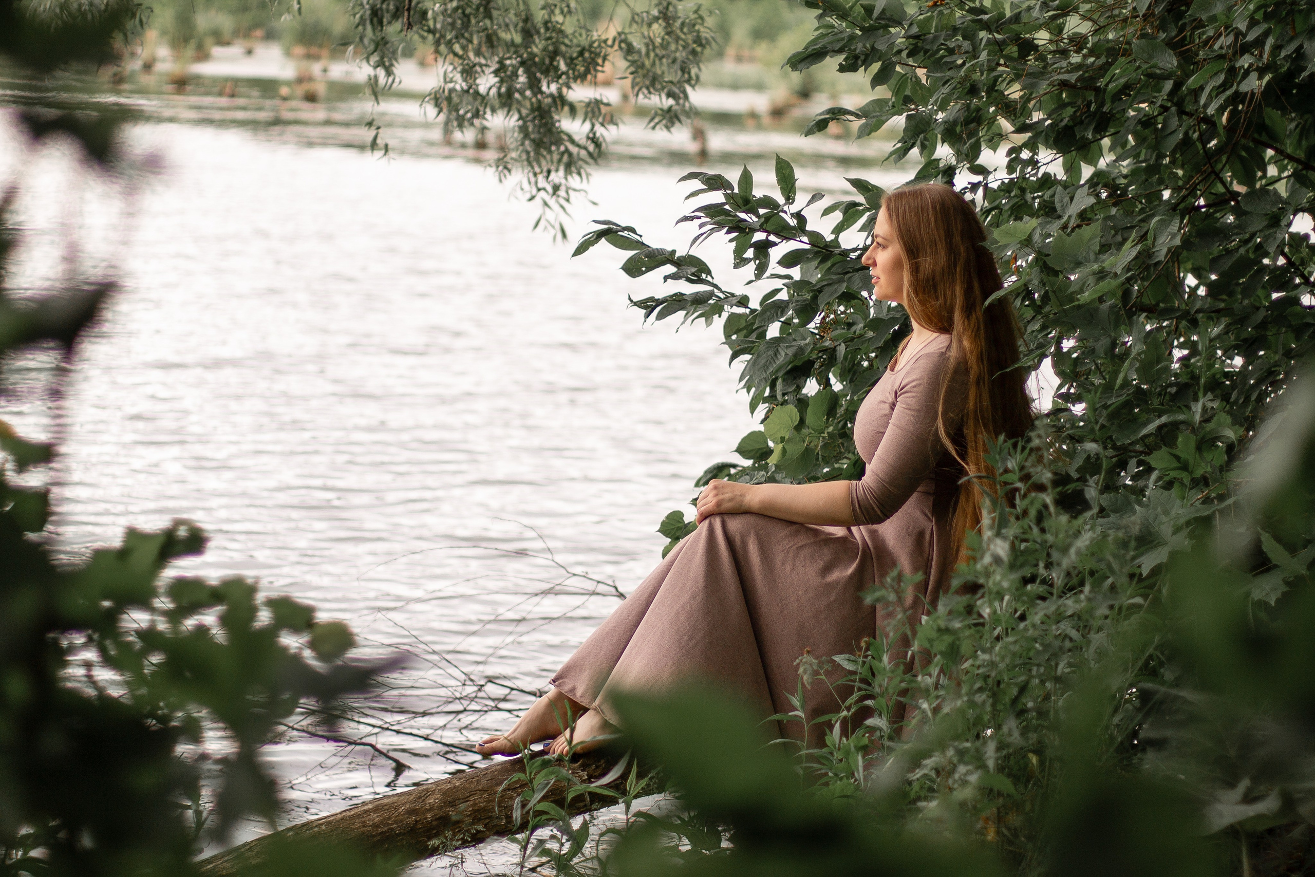 Фотосессия девушки летом, девушка с длинными волосами сидит на берегу реки