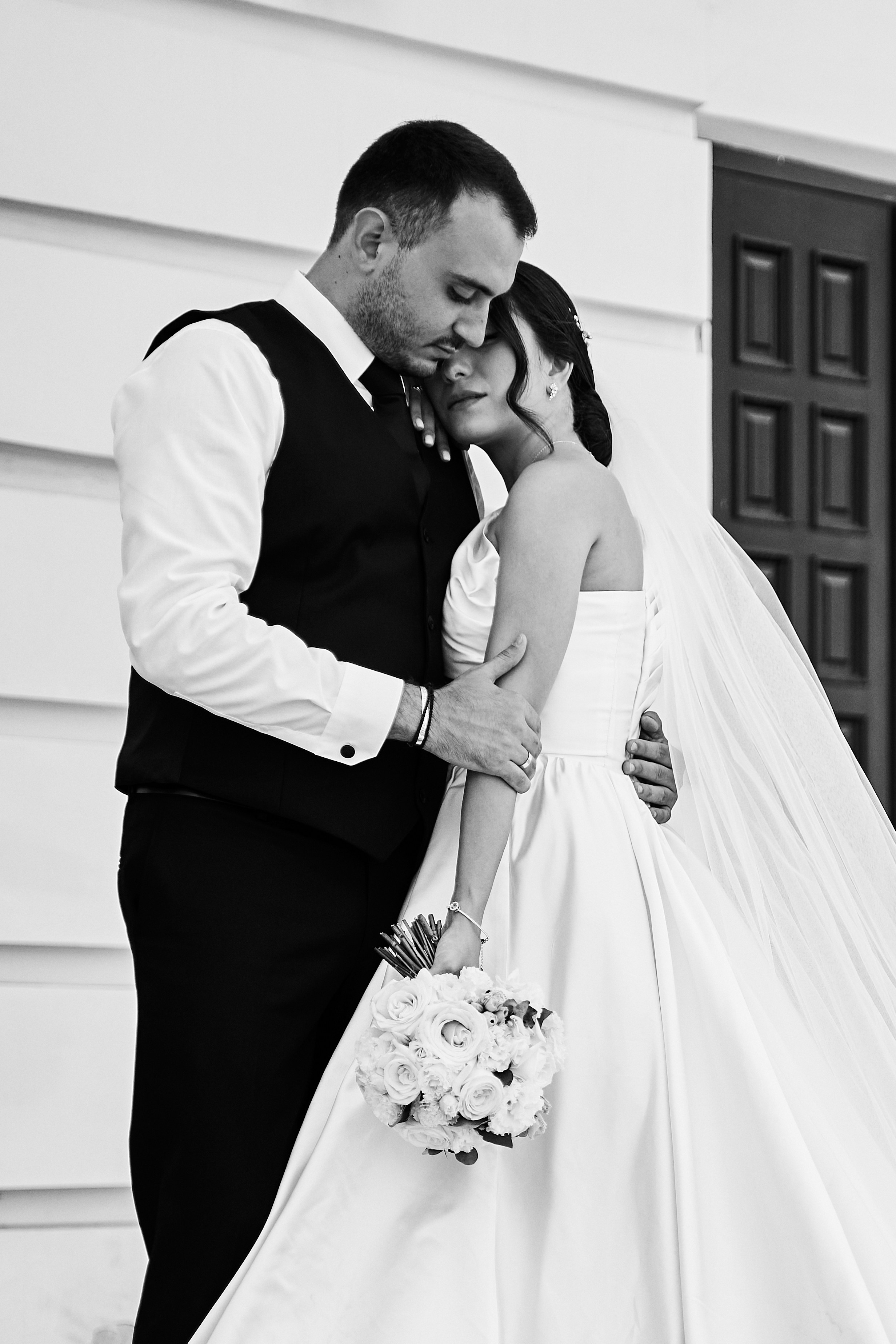 жених обнимает невесту у колон, черно-белое фото