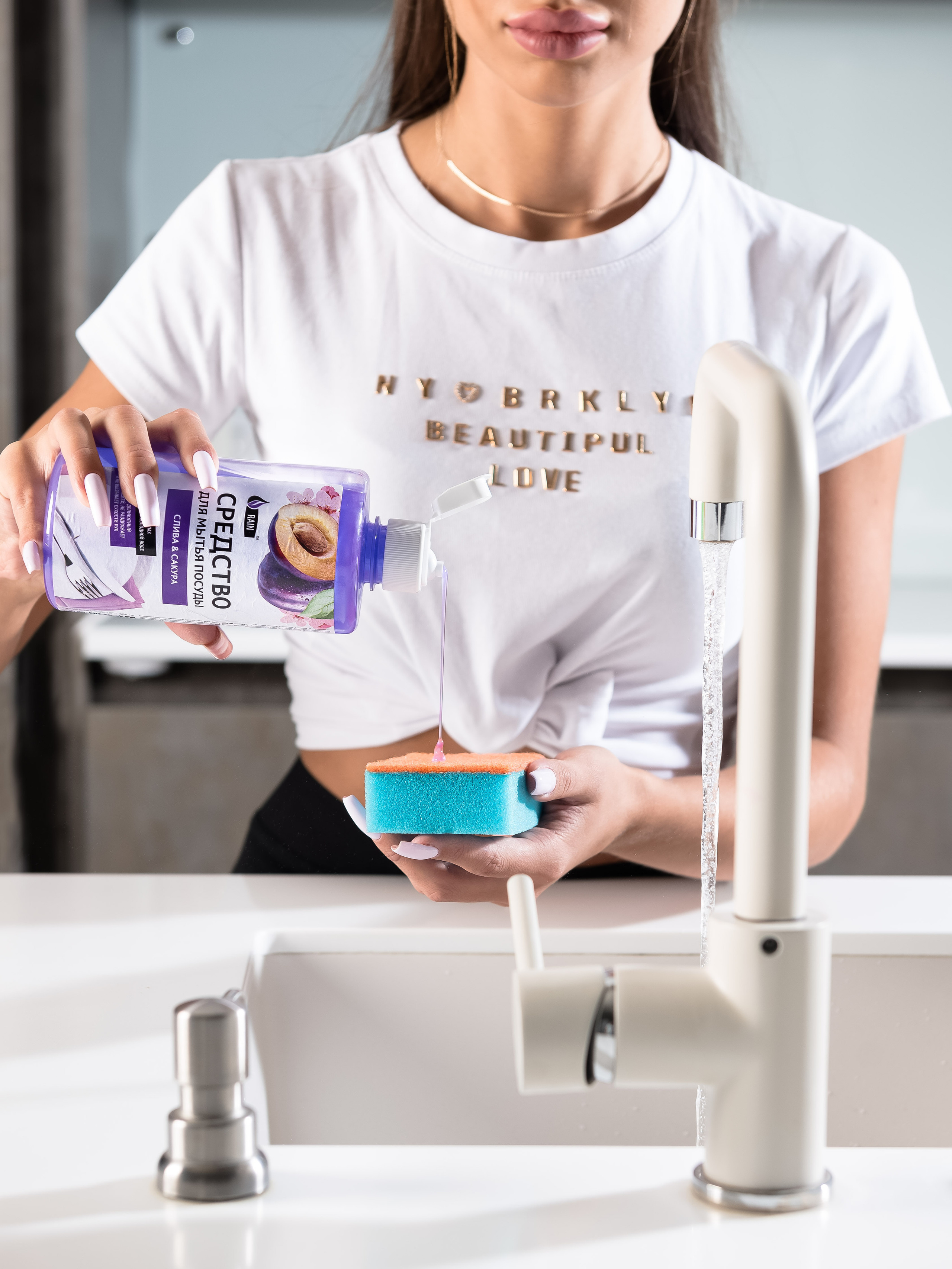 Средство для мытья посуды в руках девушки, на переднем плане кран раковины и бежит вода.