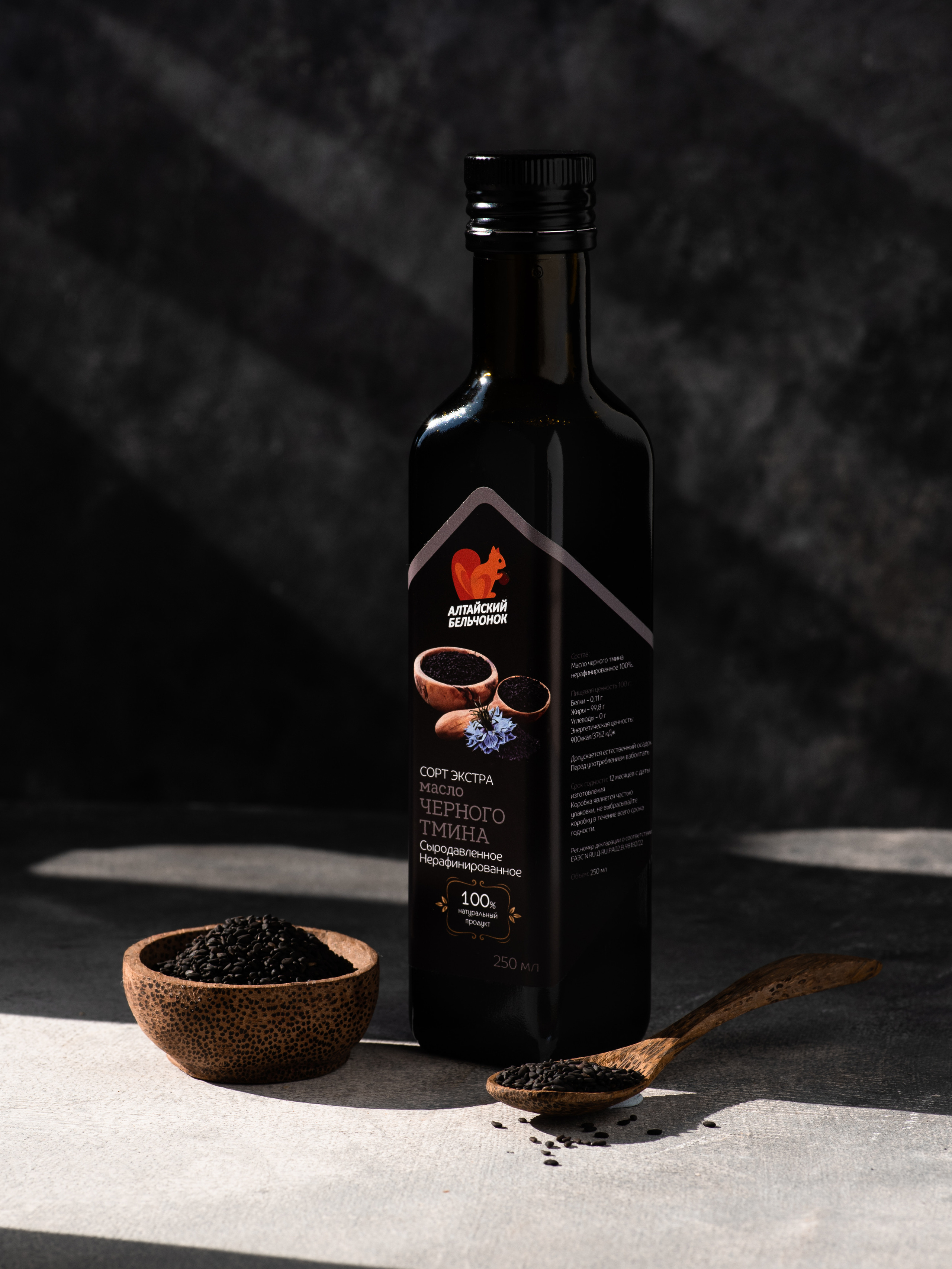 Фото масла из черного тмина на темно-сером фоне с интересным свето-теневым рисунком