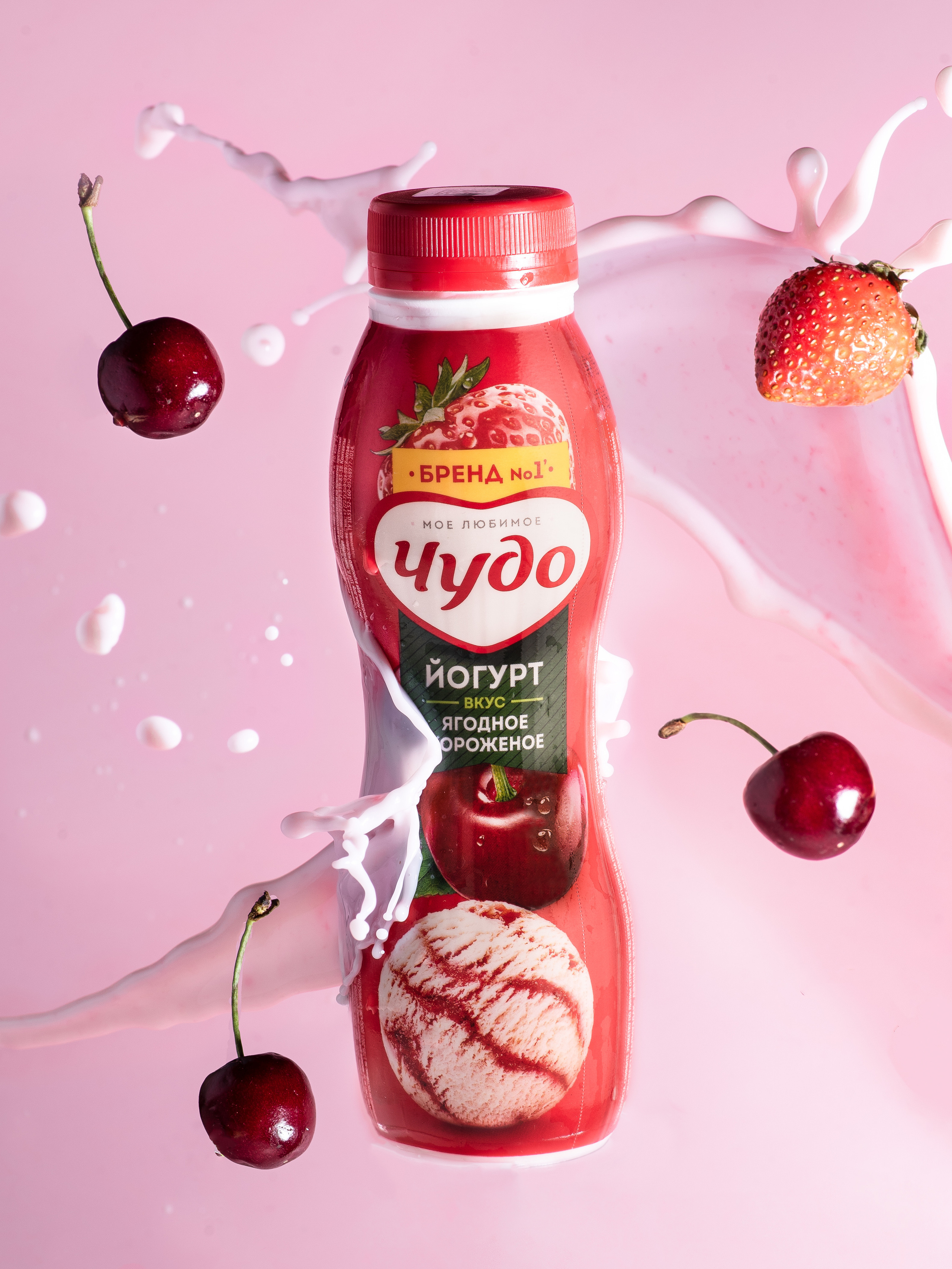 Бутылка ягодного йогурта Чудо на розовом фоне в брызгах йогурта и летящих ягод
