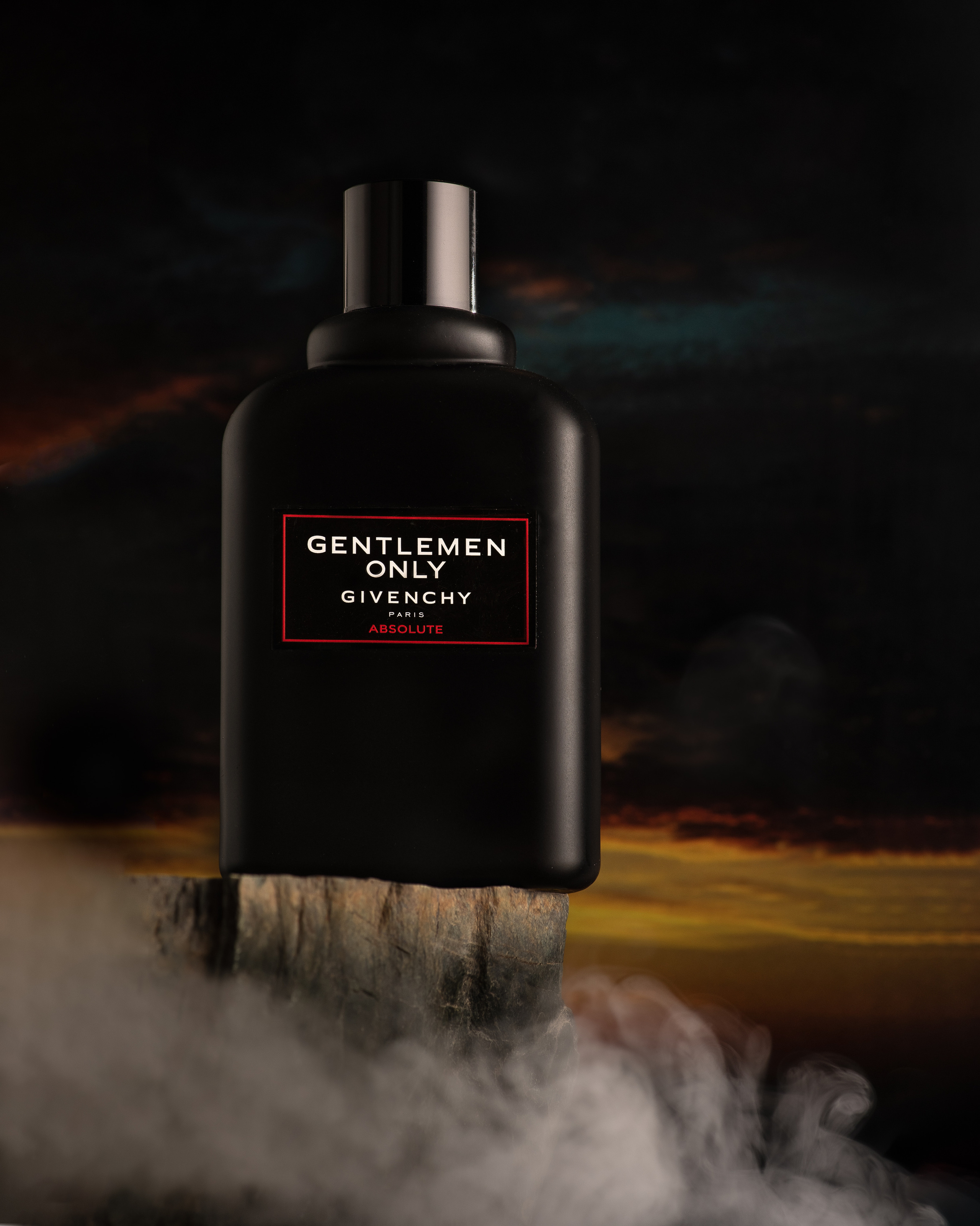 Мужские духи на фоне закатного неба на скале с дымом от облаков