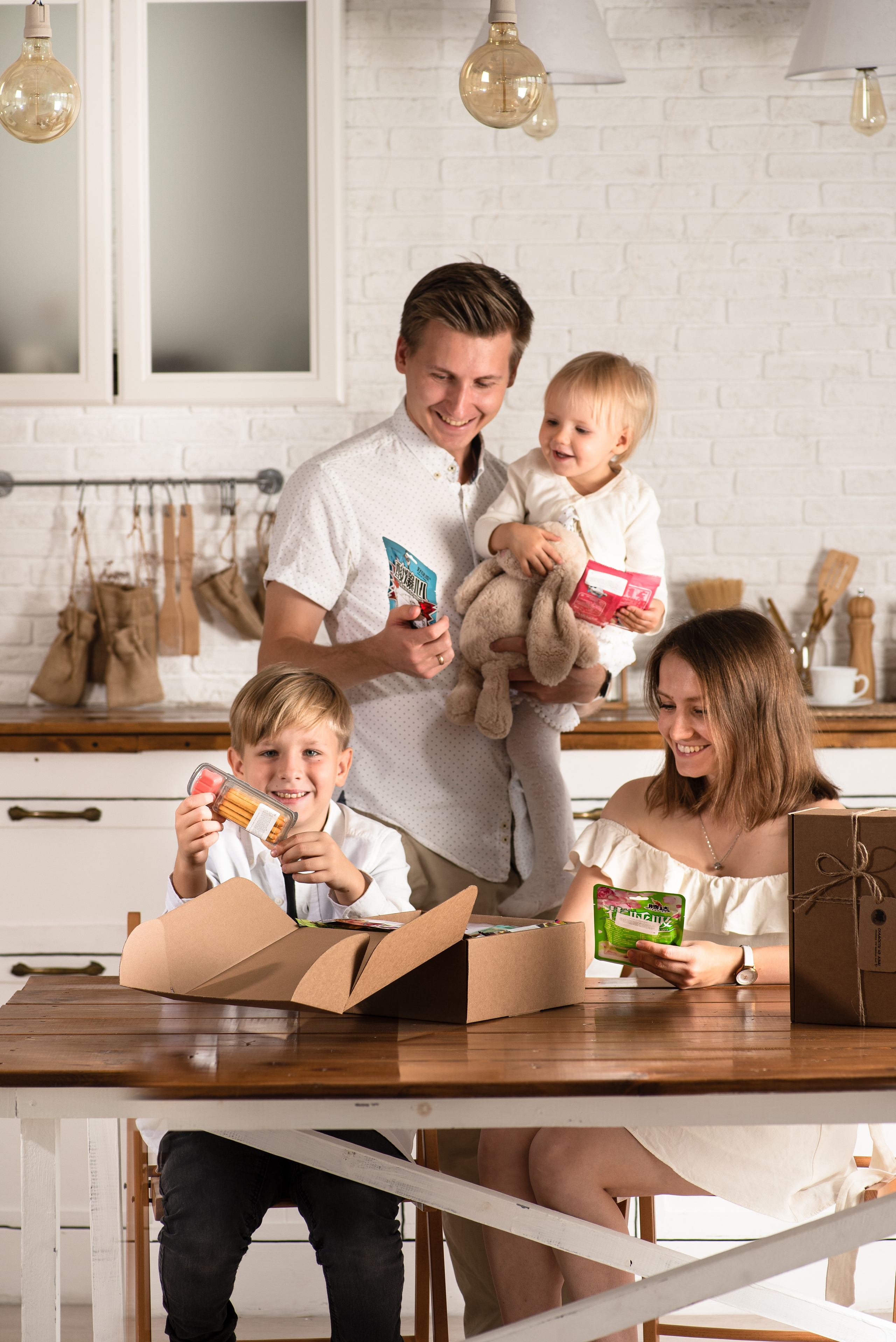 Красивая семья блондинов из 4 человек на светлой кухне открываюь коробку конфет и радуются