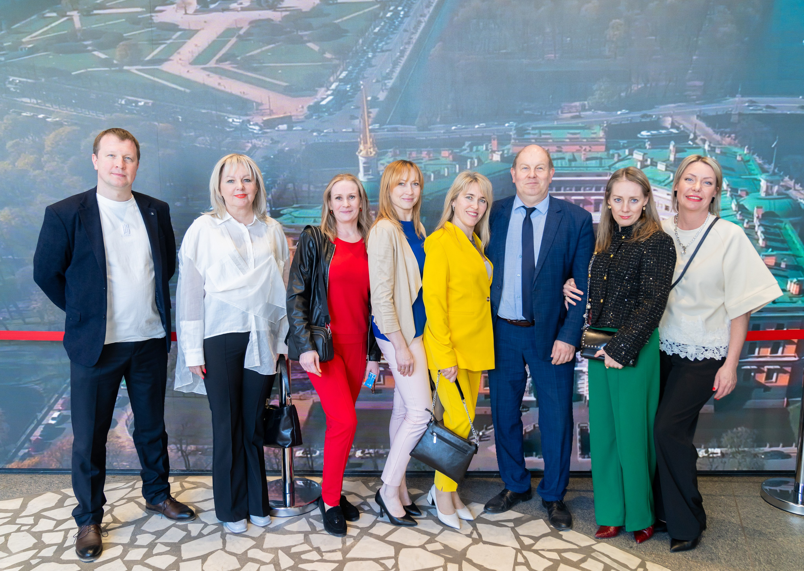 Групповое фото участников Дня местного самоуправления Санкт-Петербург. Семь человек в деловой одежде перед большой городской панорамой. Фото Евгения Мальцева