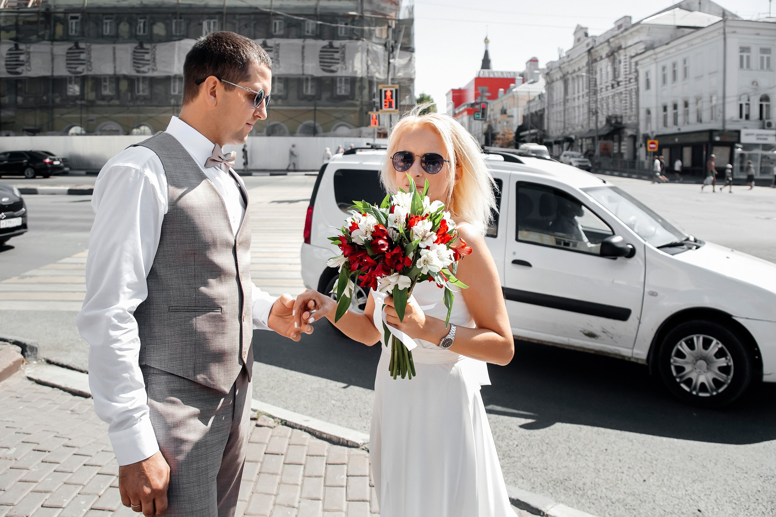 свадебная прогулка в городе, жених и невеста прогуливаются по центральной улице, мимо проезжают машины