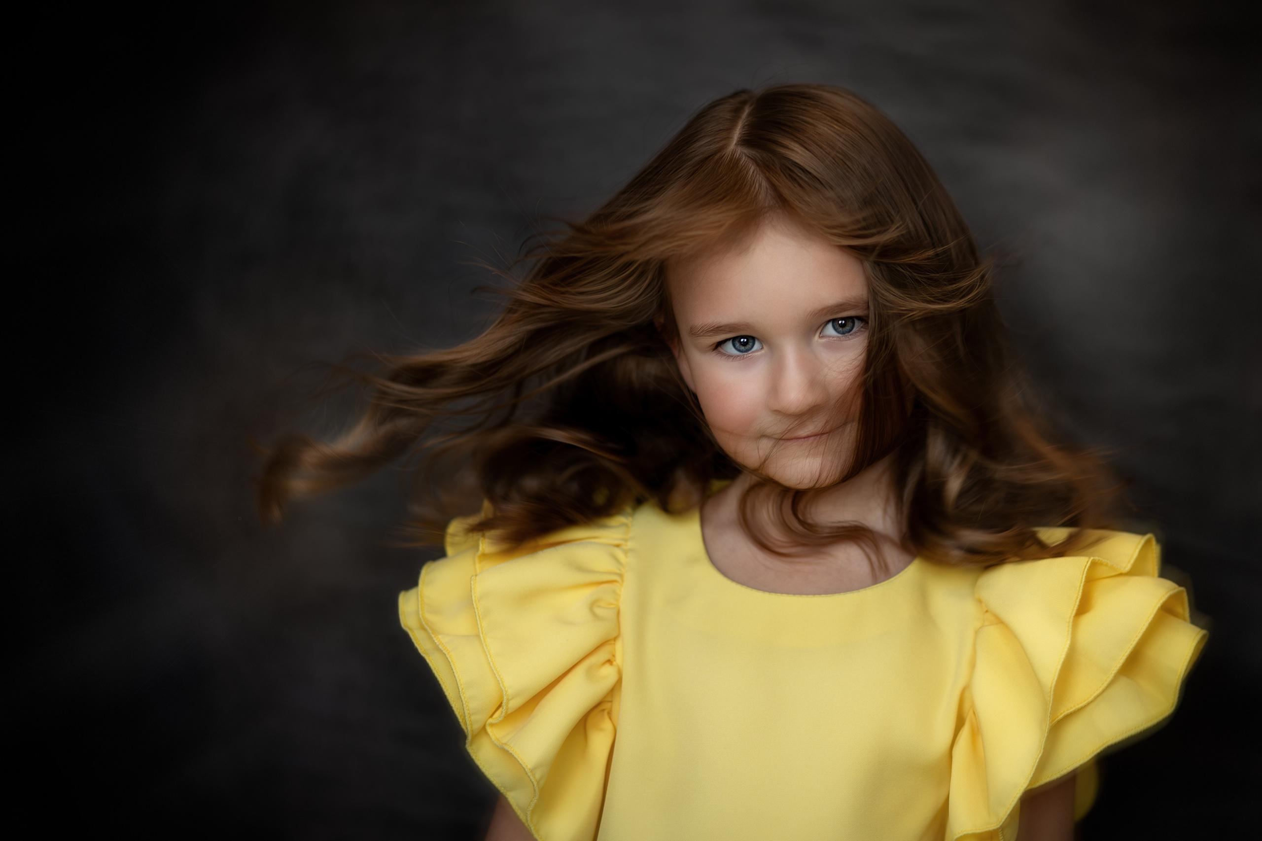 Портрет девочки с голубыми глазами в жёлтом платье, волосы развеваются, мягкий свет, тёмный фон
